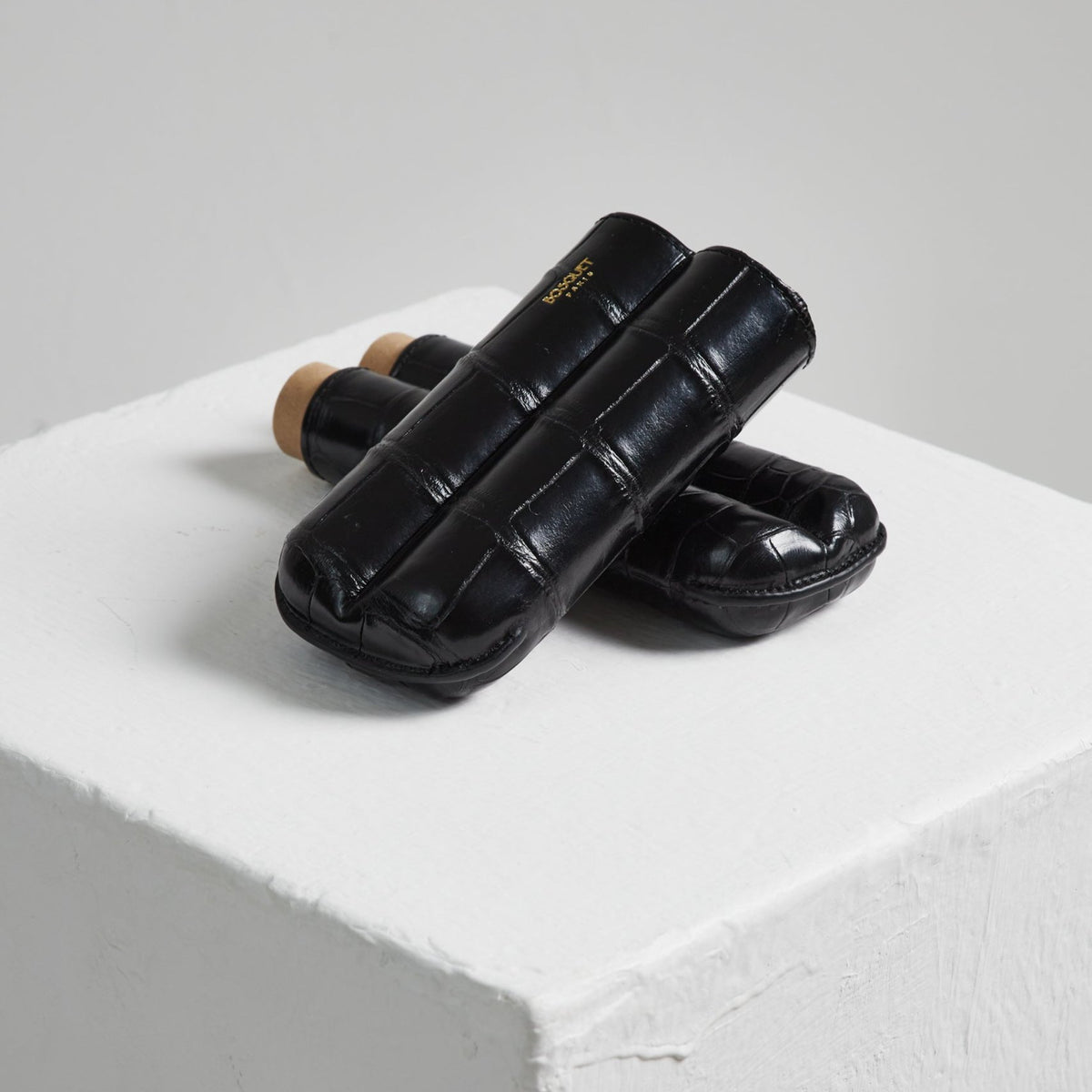 A pair of Bosque black shoes on top of a white cube made of Bosquet Crocodile Cigar Case, Black leather.