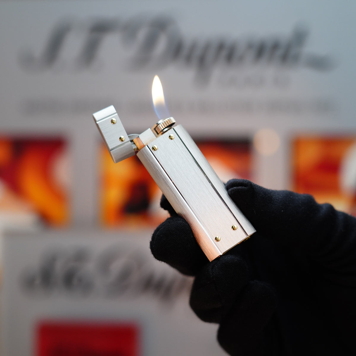 A gloved hand holds a lit 1982 Cartier Santos Palladium Two Tone lighter with solid 18k gold screws, set against a blurred background, highlighting the elegant design of this large-sized piece.