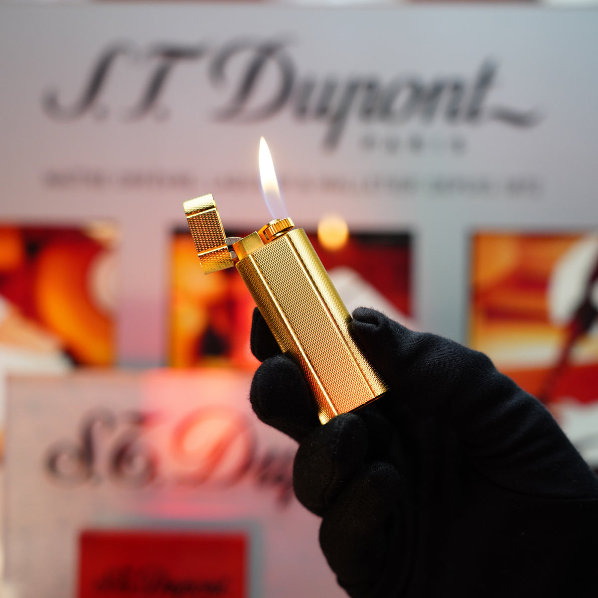 A gloved hand holds a collectible item with a lit gold lighter in front of a blurred background, showcasing the Cartier logo's elegance and sophistication on the Vintage 1980 Le Must Fine Hobnail & Lines Pattern Lighter with 24k Gold Finish.