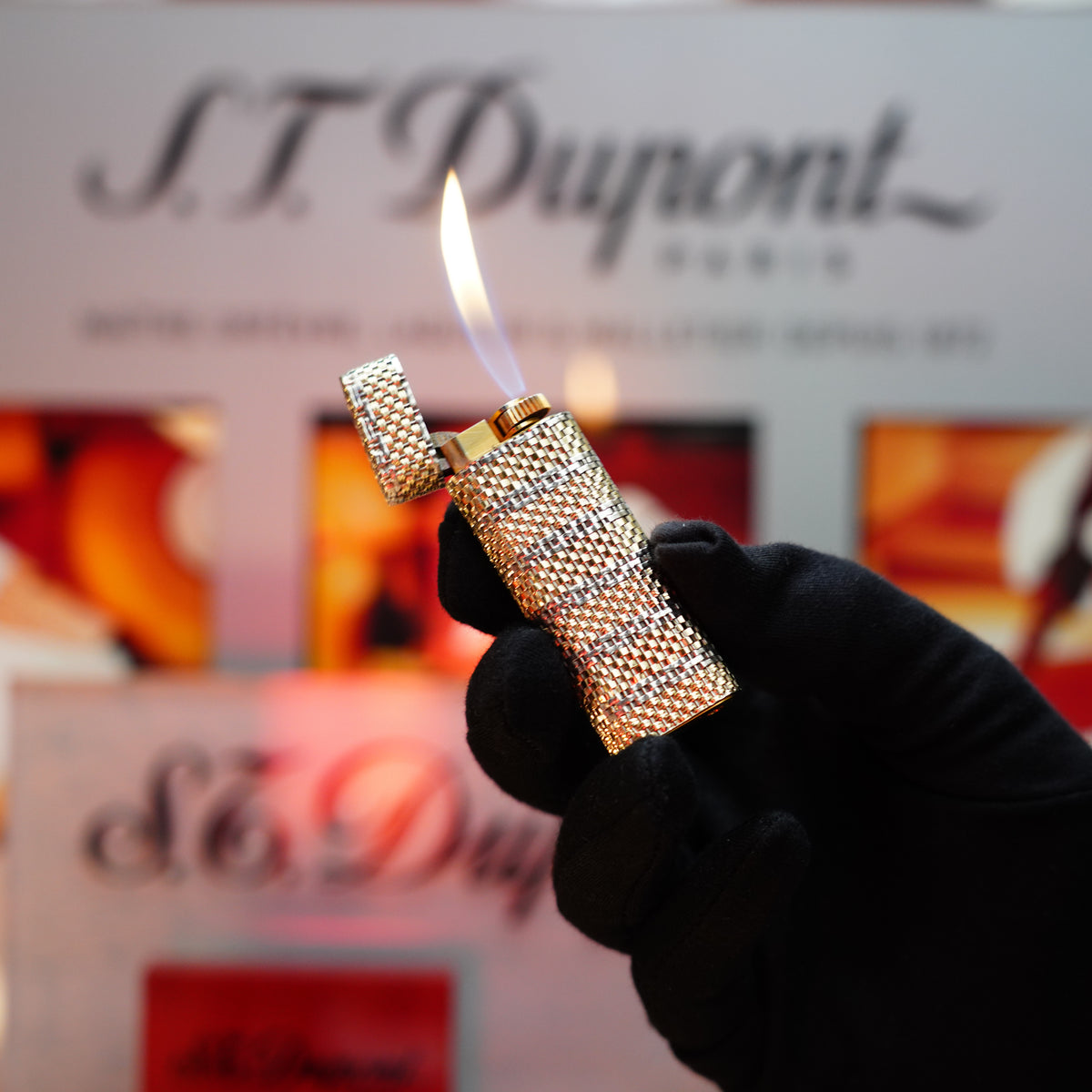 A gloved hand holds a Vintage 1980 Cartier Solid 18k Gold Basket Jacket lighter, adorned with the 750 hallmarks, against a blurred S.T. Dupont background—an extraordinary collector's item reminiscent of timeless artistry.