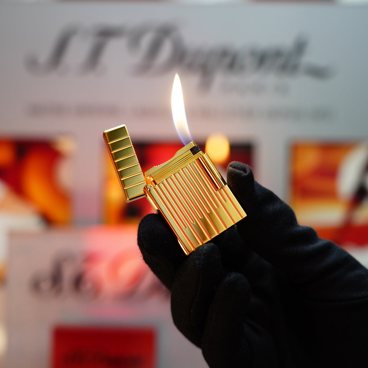 A hand in a black glove holds an open S.T. Dupont Vintage 1990 Ligne 1 Lighter with a heavy 24k gold finish and double lines pattern, its flame flickering against a blurred background.