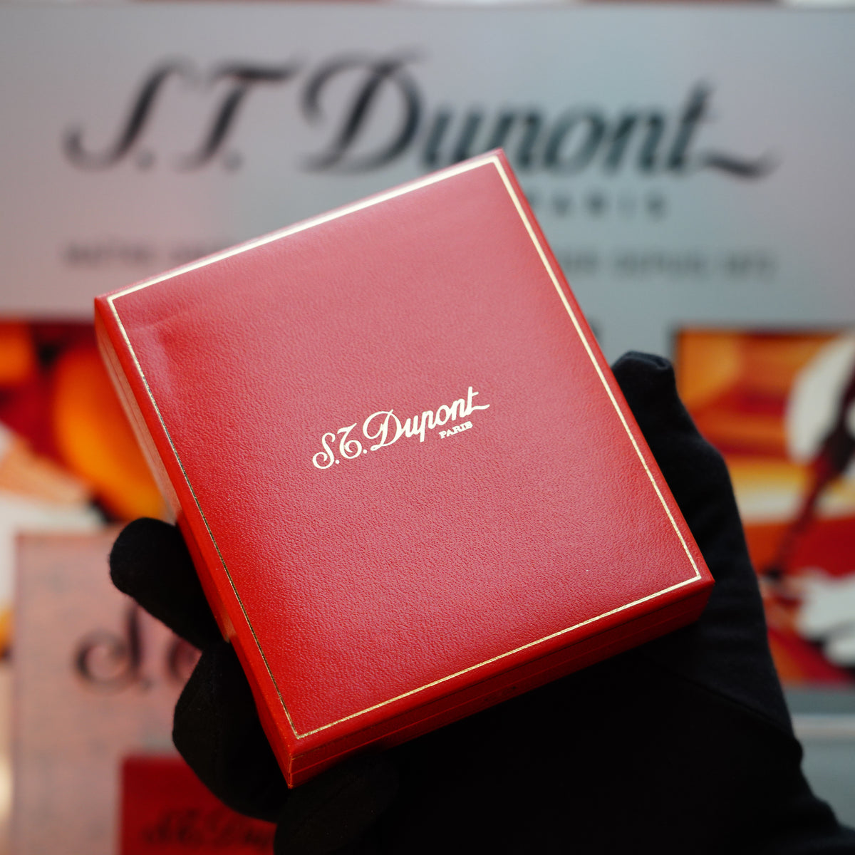 A gloved hand holds an S.T. Dupont Paris box with gold trim, showcasing a Vintage 1990 St Dupont Ligne 1 lighter in a striking 24k gold finish and featuring a double lines pattern.