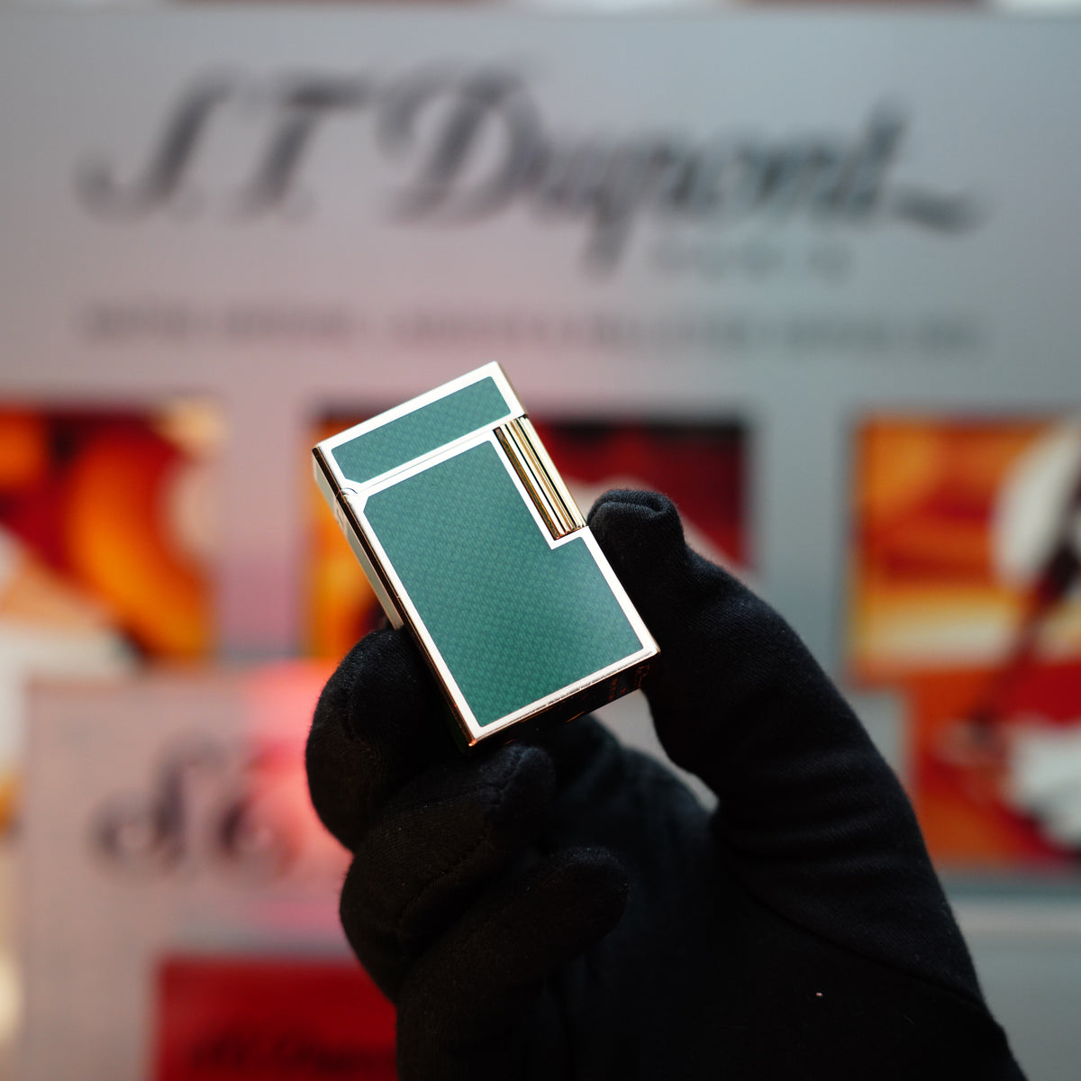A gloved hand holds a Vintage 1990 S.T. Dupont Contemporaine Ligne 1 Green Vert Filet Plaq Lacquer Lighter with a 24k Gold Finish, set against a blurred background with indistinct text.