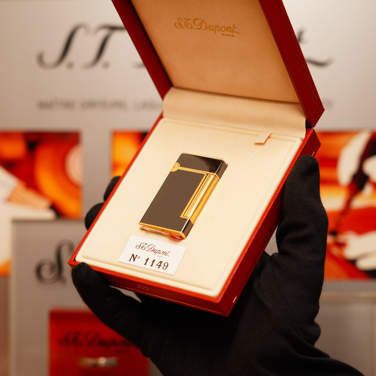 A gloved hand showcases a Vintage 1990 S.T. Dupont black lacquer and gold Ligne D lighter, elegantly displayed in an open red case.