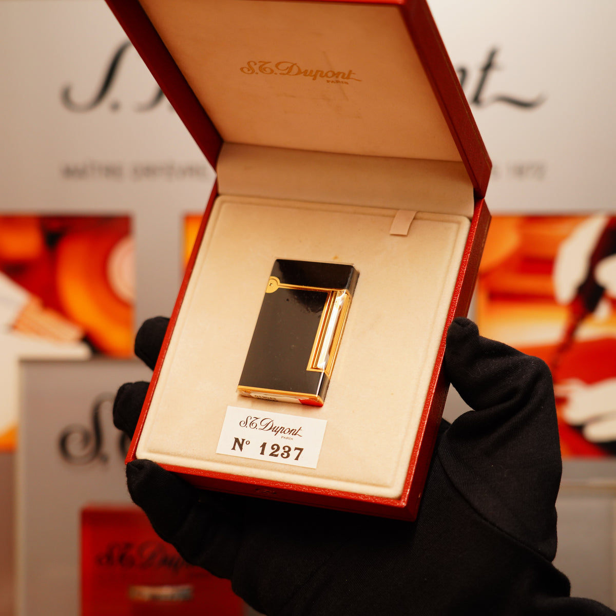 A gloved hand holds an S.T. Dupont Vintage 1990 Overall Black Lacquer Early 24k Gold Ligne D Sealed Lighter in a red box, labeled with the number 1287.