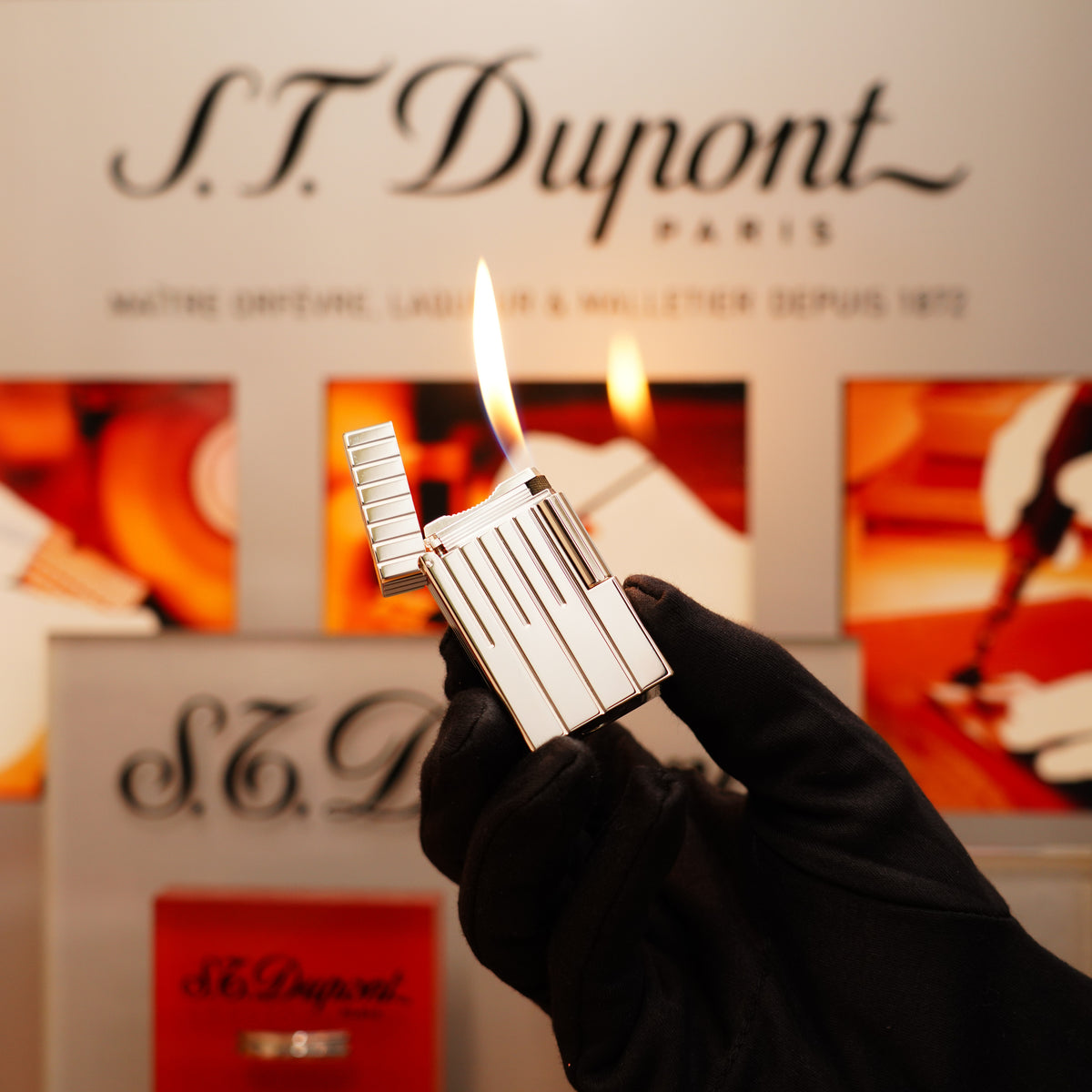 A hand in a black glove holds a lit Vintage 1999 S.T. Dupont Grand Master Perspective 2000 Palladium Plated Lighter, displaying a blue and orange flame.