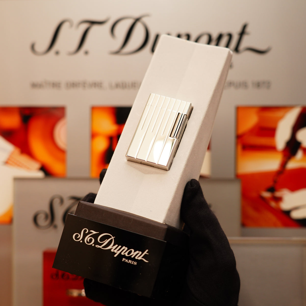A black-gloved hand holds a white box with a Vintage 1999 S.T. Dupont Limited Grand Master Perspective 2000 Palladium Plated Lighter, with the "S.T. Dupont" brand visible in the background.