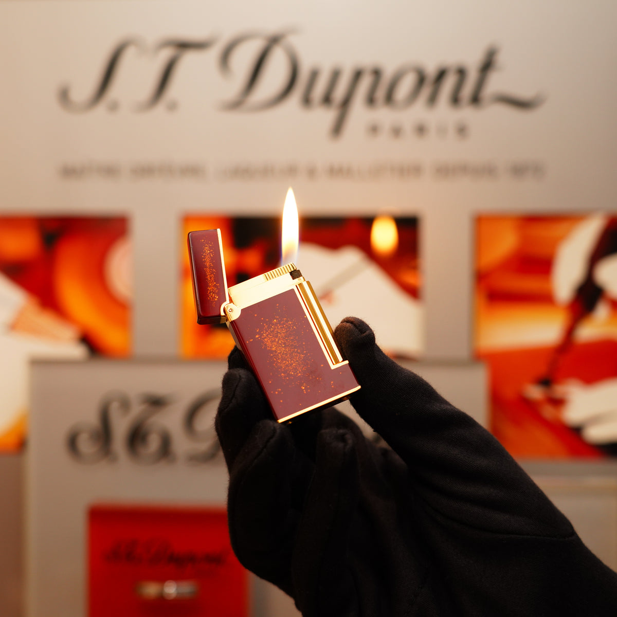 A gloved hand holds an open, lit S.T. Dupont Vintage 1980 StarDust Ligne 2 LD lighter with a speckled purple design, against a blurred branded background.