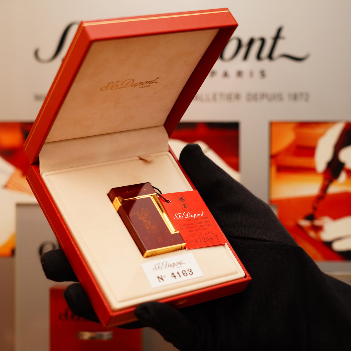 A gloved hand holds an open red box containing a Vintage 1980 S.T. Dupont StarDust 24k Gold Finish Red Natural Lacquer Gold Powder Ligne 2 LD Lighter.