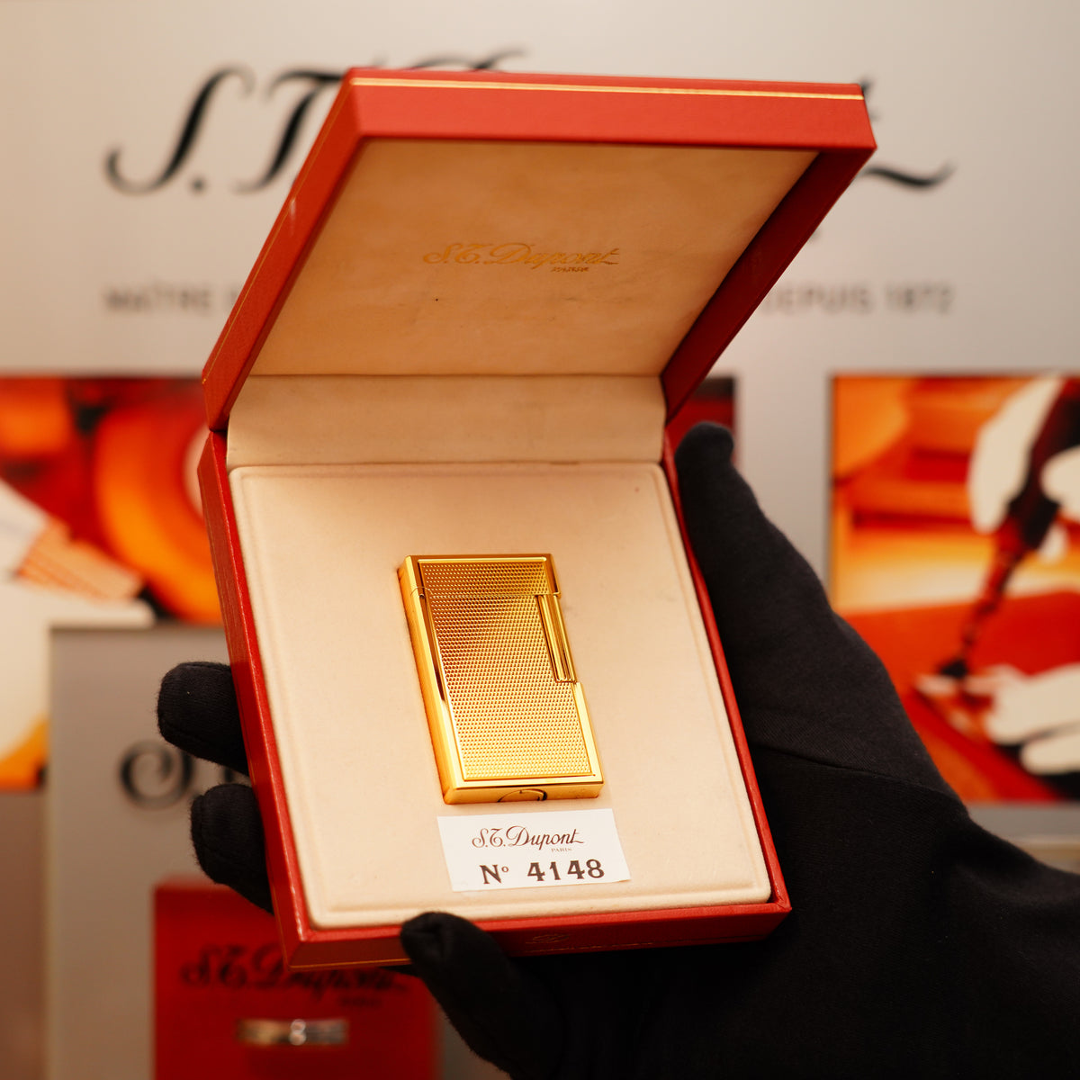 A golden S.T. Dupont lighter labeled "N° 4148" is displayed in a red box, opened by a gloved hand.