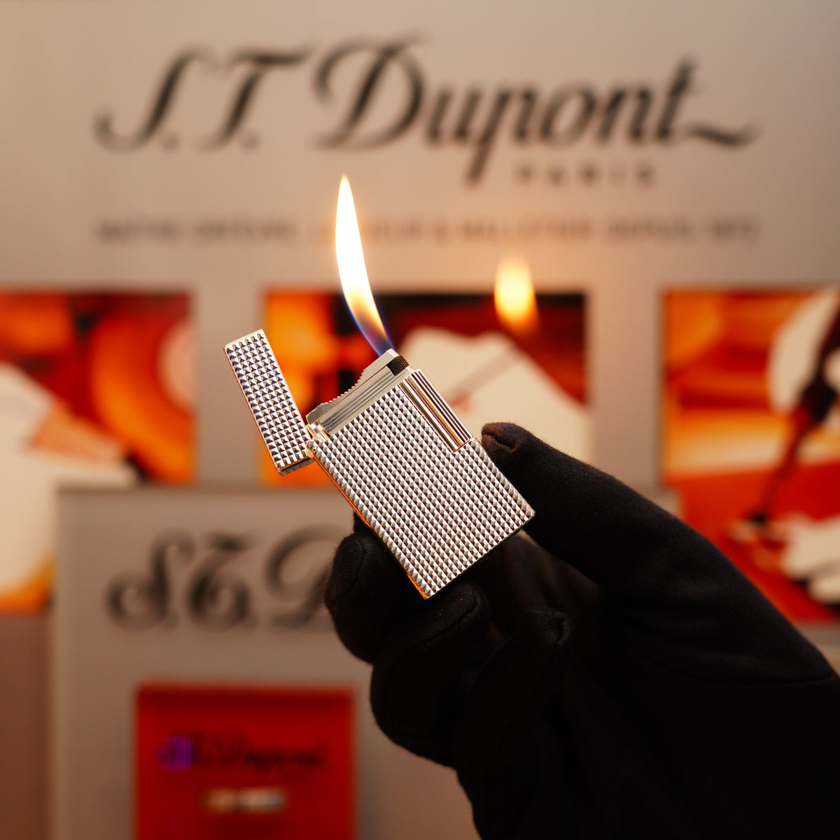 A gloved hand holds an open Vintage 1996 S.T. Dupont Ligne 1 Diamond Head Pattern Large Heavy Silver Finish Lighter, showcasing its lit flame against a blurred background displaying "S.T. Dupont Paris.