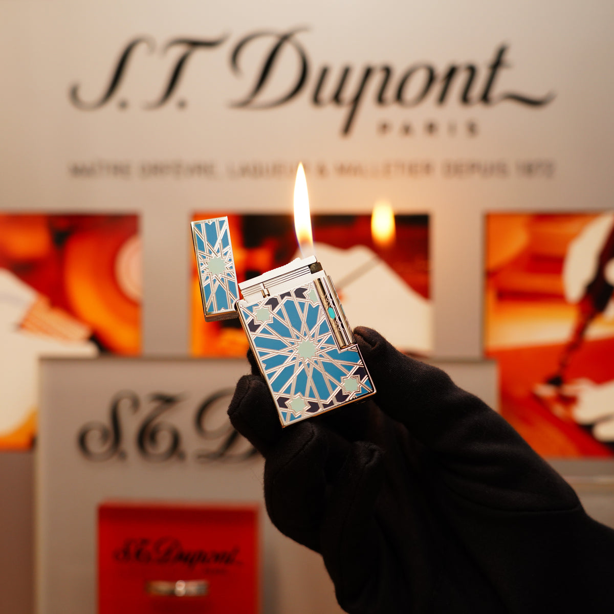 A gloved hand holds a Vintage 2003 St Dupont Andalusia Limited Edition SkyBlue Natural Lacquer Heavy Platinum Large Ligne 2 Lighter, igniting a flame. The S.T. Dupont logo is visible in the blurred background.