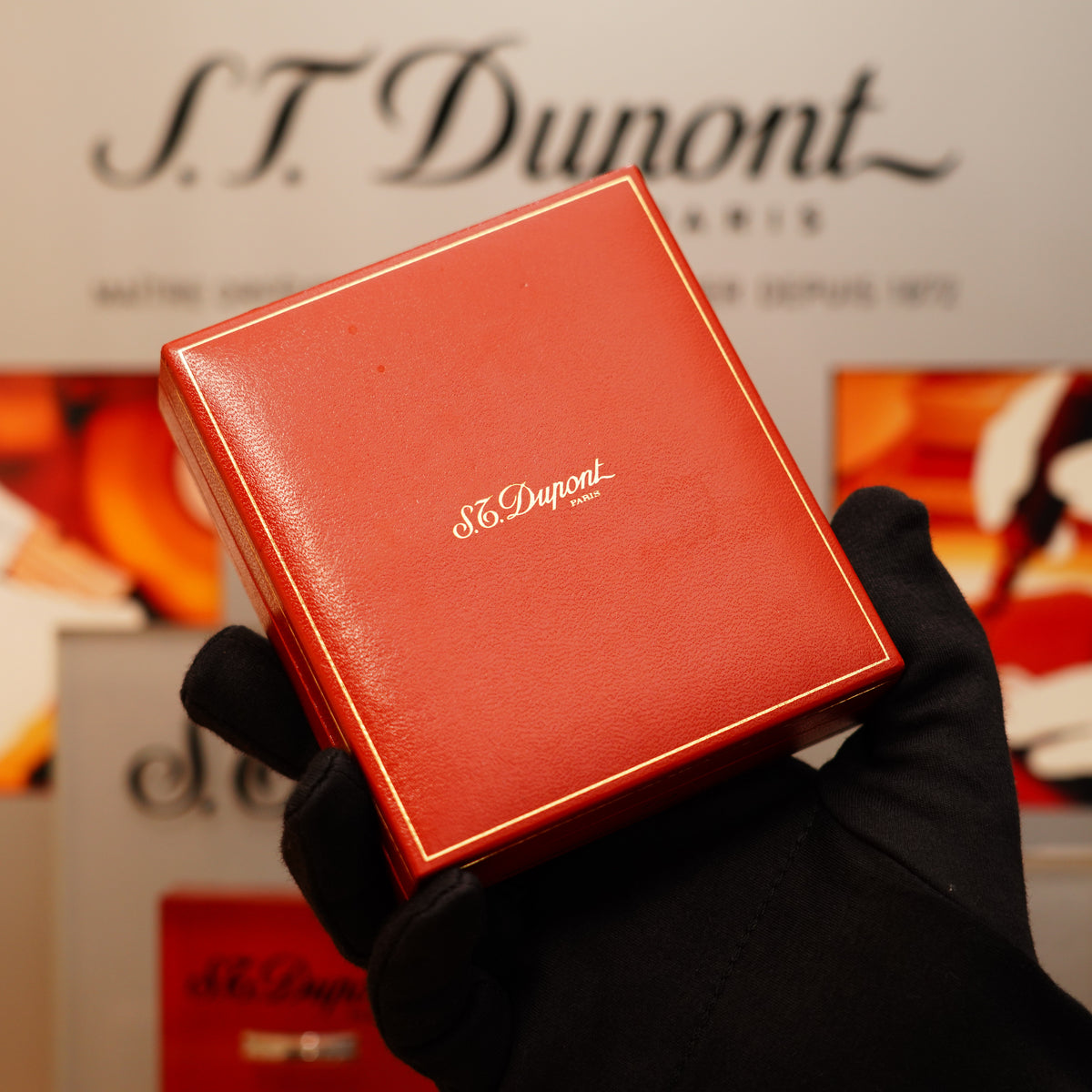 A gloved hand holds a red S.T. Dupont box against a blurred background featuring the logo, showcasing the Vintage 1990 St Dupont 24k Gold Finish small Ligne 1 rare Pattern Lighter.