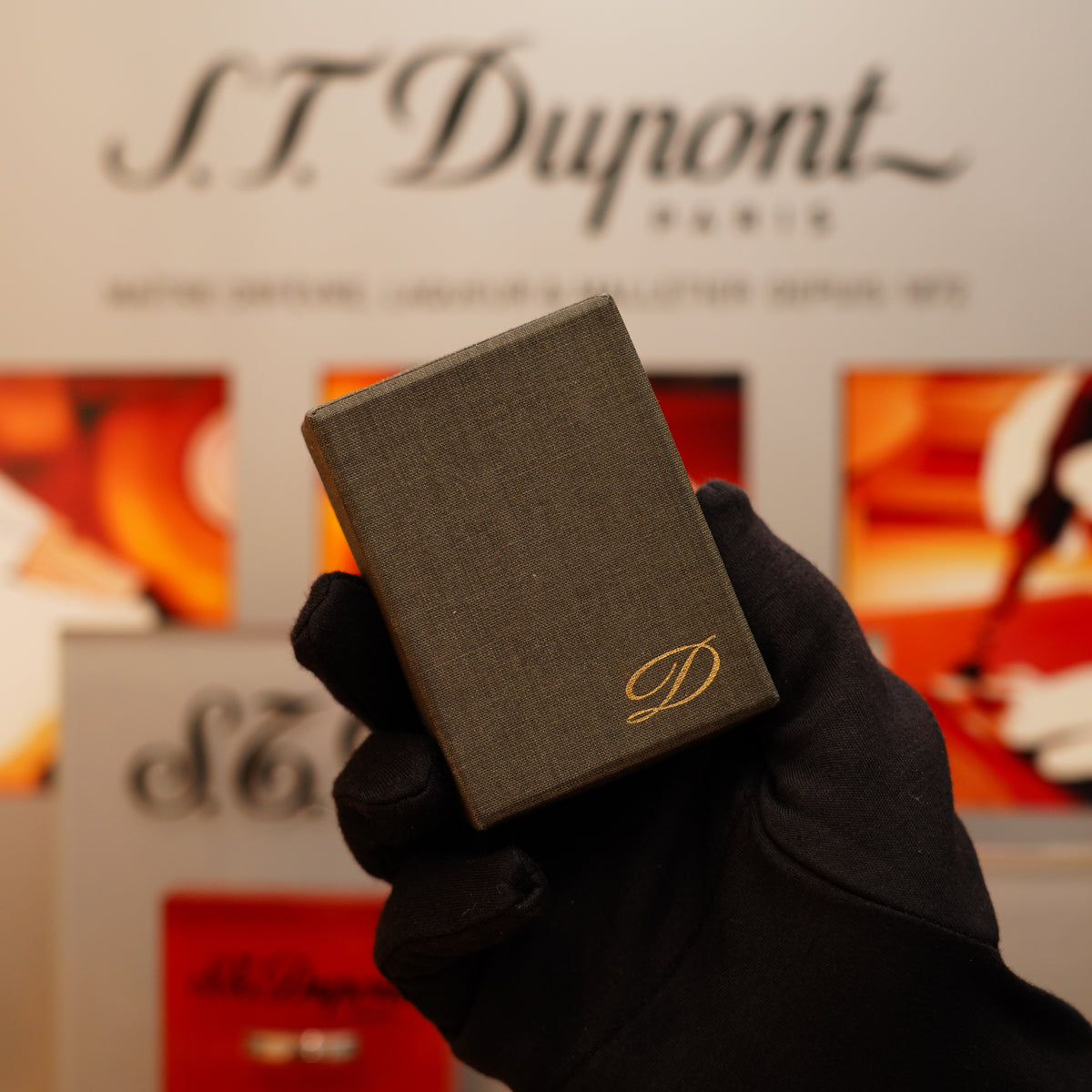 A gloved hand holds a Vintage 1973 S.T. Dupont Ligne 1 lighter with a gold "D" emblem, while the S.T. Dupont branding appears blurred in the background.