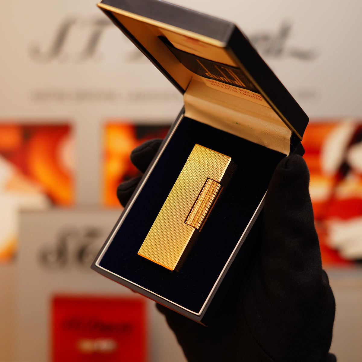 A gloved hand holding a jeweler's box reveals a Vintage 1970 Dunhill 24k Gold Finish Rollagas Diamond Head Pattern Initial Version Lighter.