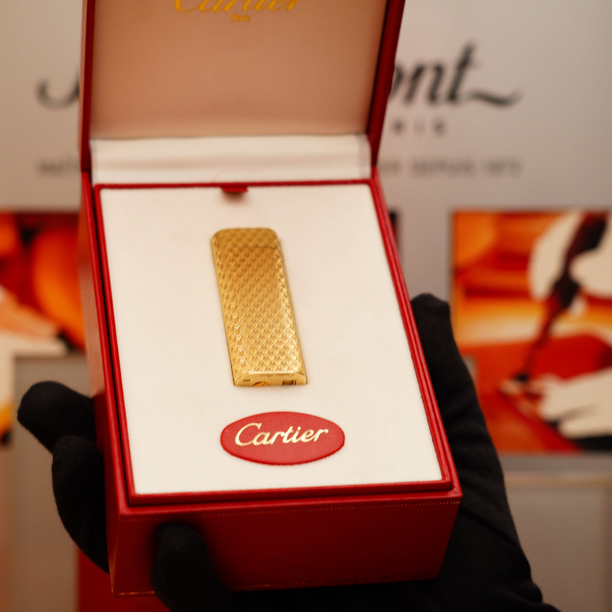 A gloved hand holds a Vintage 1970 Rare Cartier Solid 18k Gold Lighter in a red case with Cartier branding visible inside.