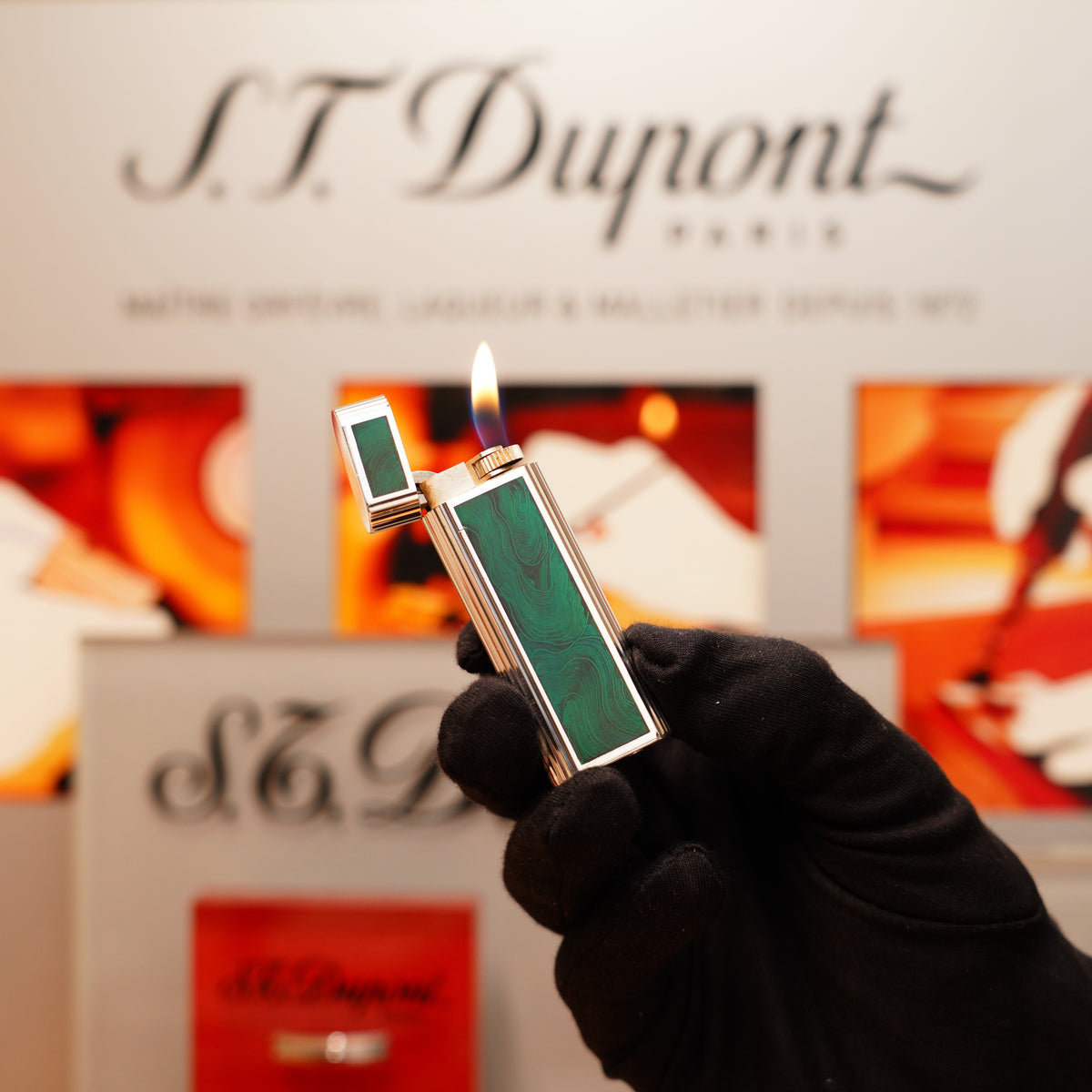 A gloved hand holds a lit Vintage 1970 Extremely Rarest Cartier Solid Sterling Silver lighter featuring a green enamel design, with the Cartier brand visible in the background.