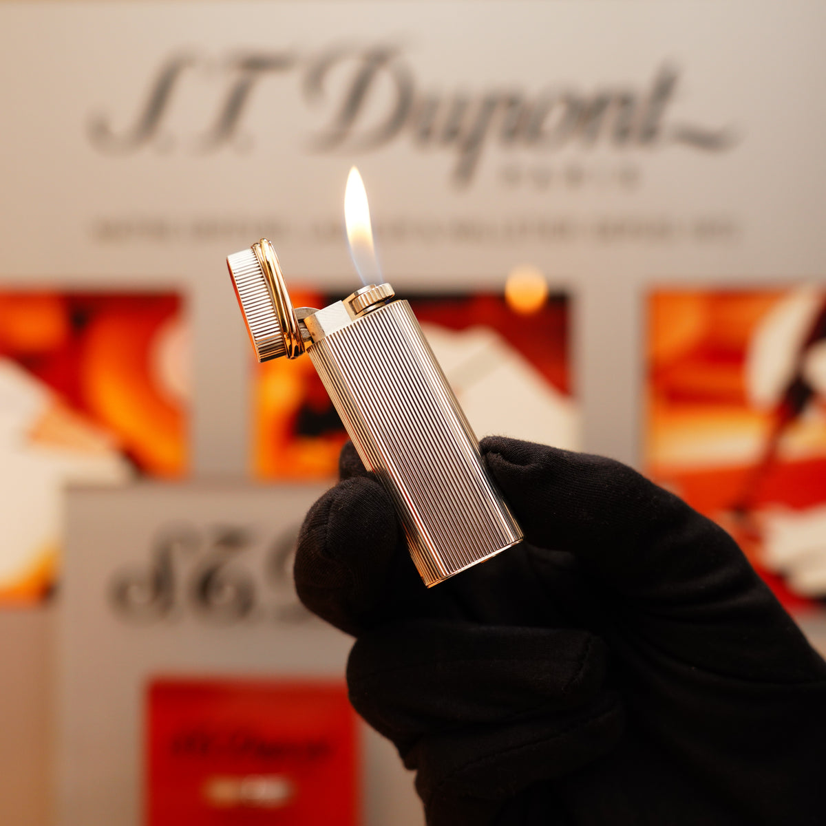 A hand in a black glove holds a lit Vintage 1970 Extremely Rare Cartier Solid 925 Sterling Vertical Line with Solid 18k Tirinty Love Ring Over the Door Factory Lighter against a blurred background.