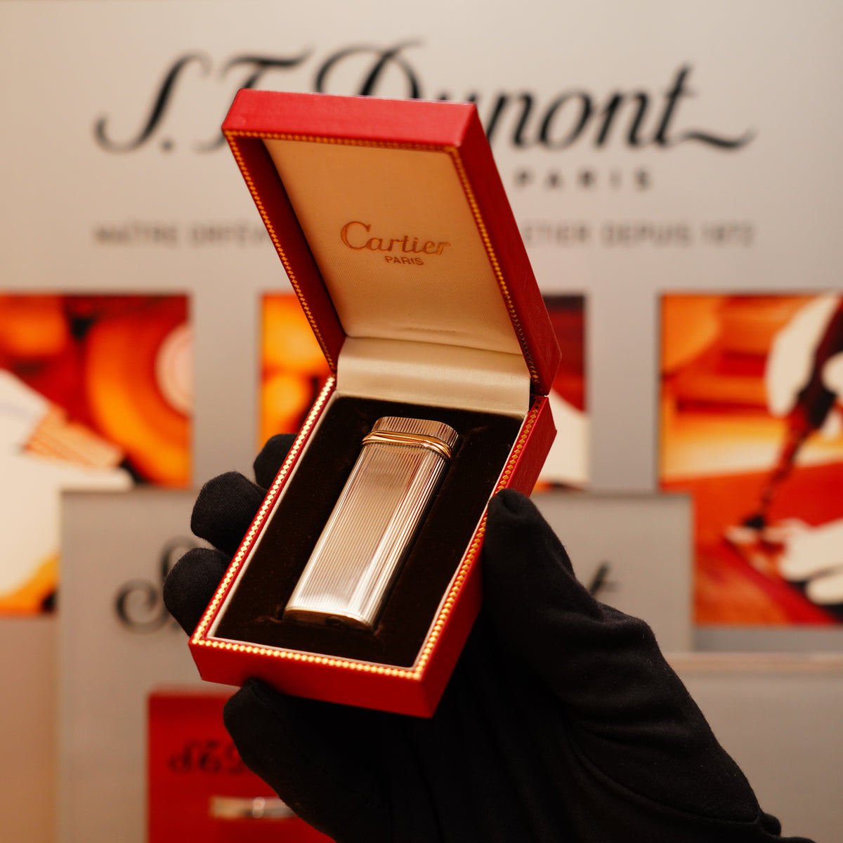 A gloved hand holds an open red box displaying a Vintage 1970 Extremely Rare Cartier Solid 925 Sterling Lighter, with S.T. Dupont branding blurred in the background.