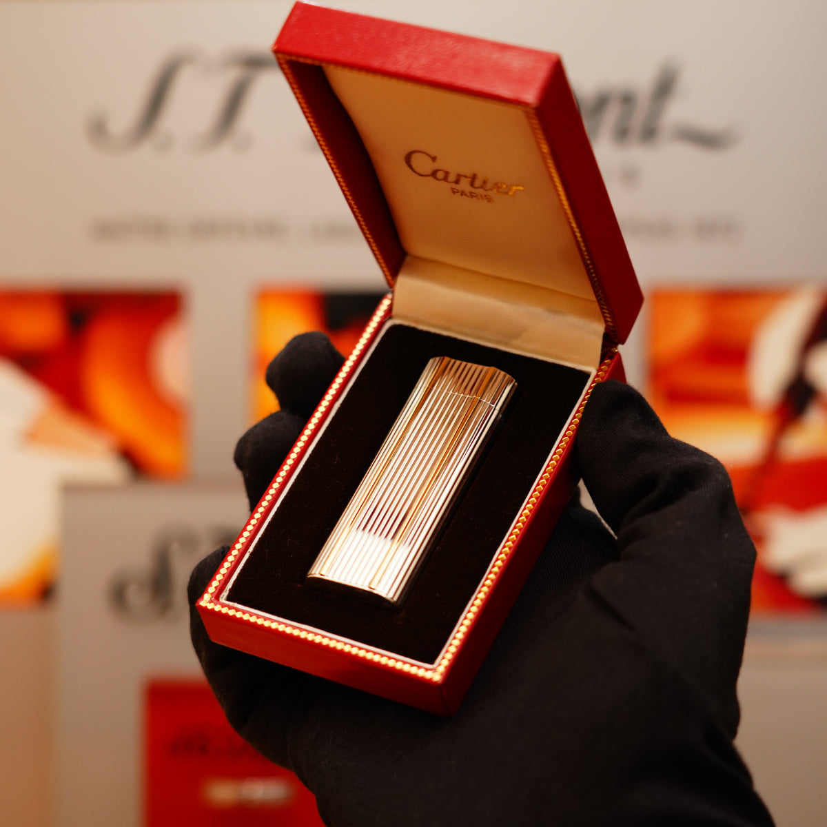 A hand in a black glove holds a Vintage 1970 Extremely Rare Cartier lighter, made of solid 925 sterling with 18k lines, in a red Cartier box with a soft interior.
