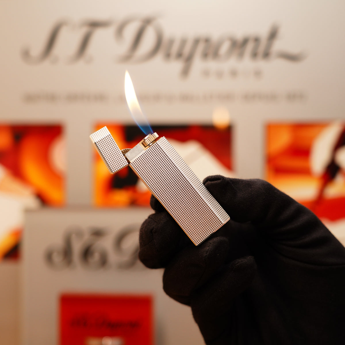 A gloved hand holds a lit Vintage 1980 Cartier Heavy Silver Finish Pentagon Lighter against a blurred background featuring the Cartier logo.