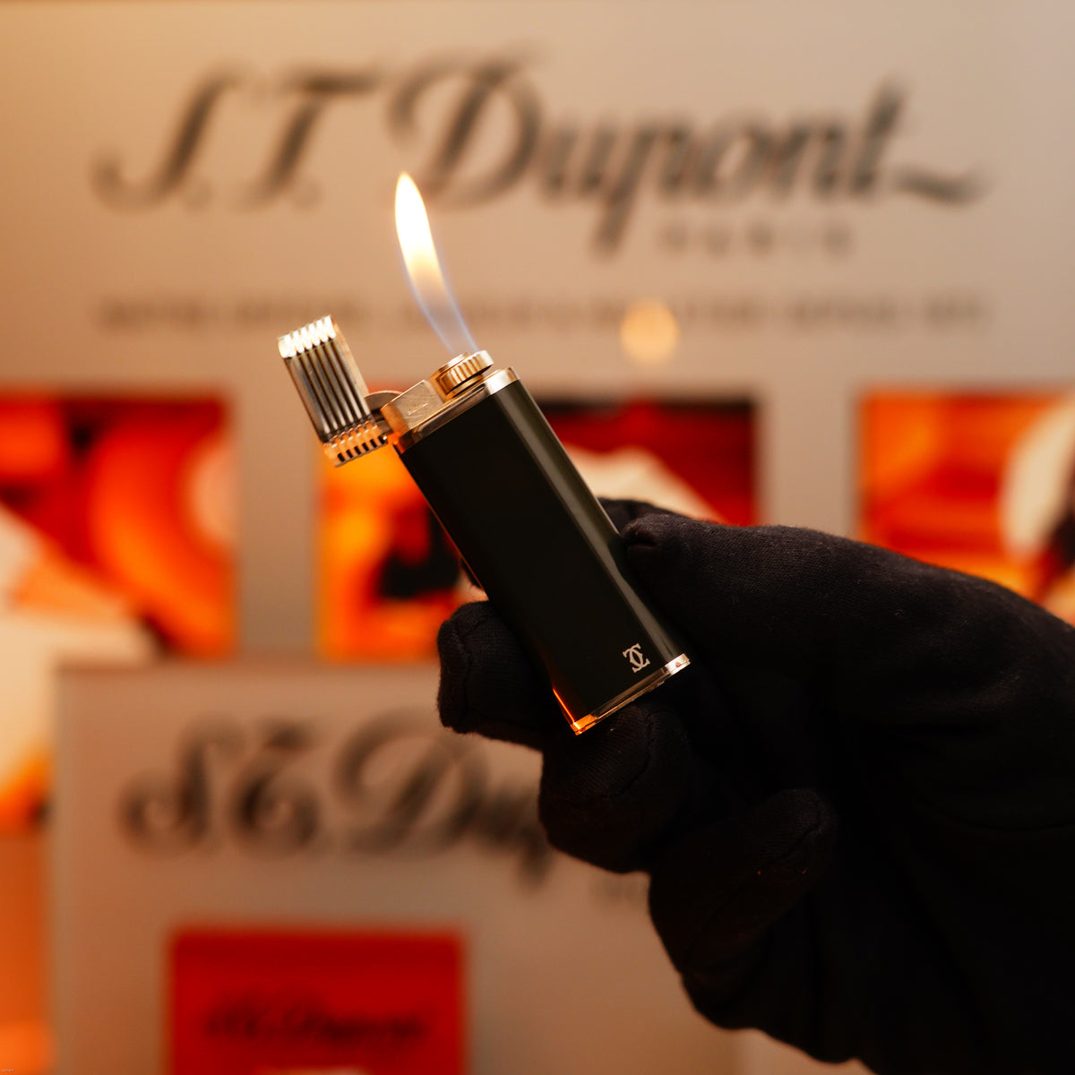 A gloved hand holds a lit Vintage 1970 Extremely Rare Cartier Solid 925 Sterling Silver Dark Green Lacquer Lighter from KirbyAllison.com in front of a blurred display background.