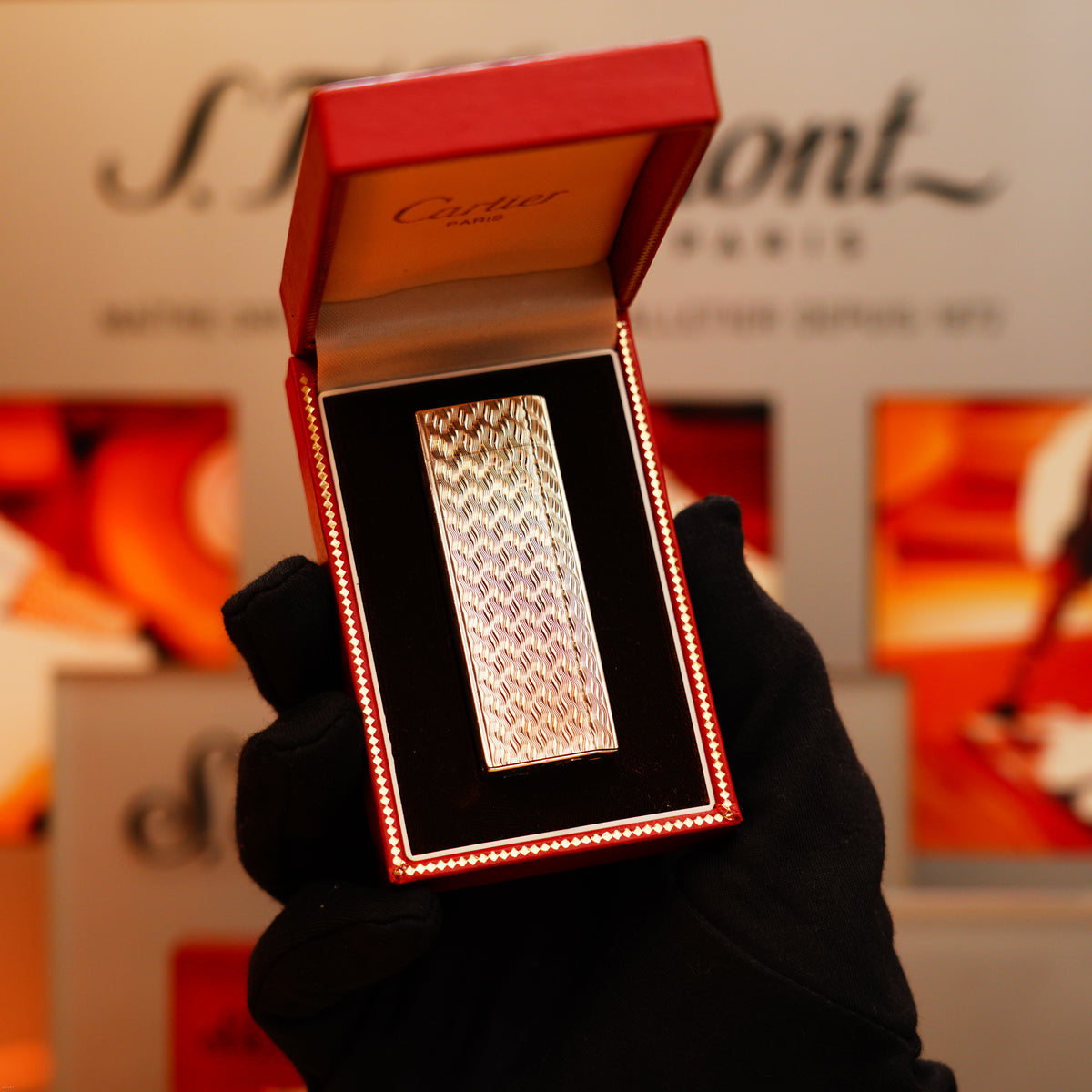A gloved hand displays a Vintage 1970 Early Cartier Production Pentagone Solid 925 Heavy Sterling Silver Lighter in an open red Cartier box against a branded backdrop.