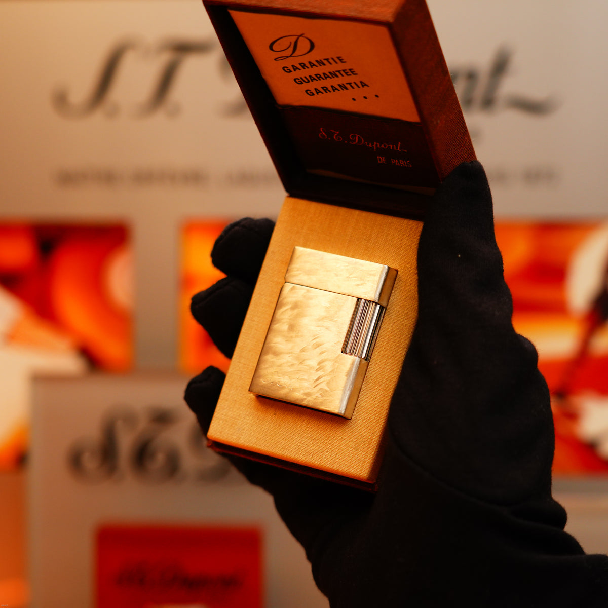 A gloved hand holds an S.T. Dupont Vintage 1970 Two Tone Solid 925 Sterling Silver Guilloché Pattern Lighter in an open box, with a warranty certificate inside the lid.