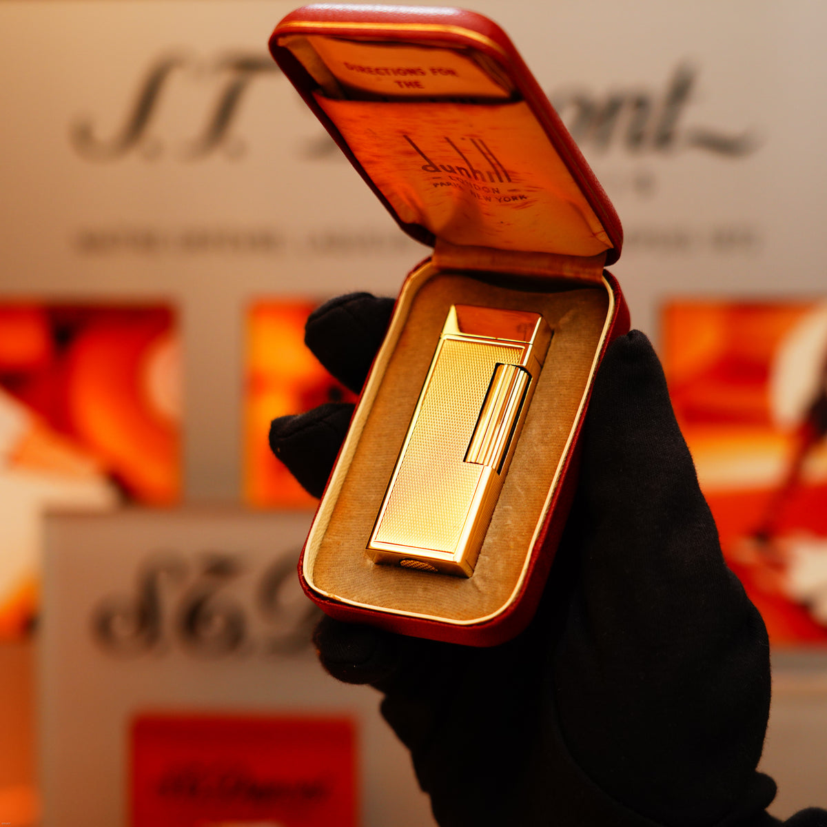 A gloved hand holds an open red case displaying a Vintage 1964 Oct. Dunhill Rollagas Early Production Solid 18k Gold Lighter (750 Hallmark, Extremely Heavy) against a blurred background.