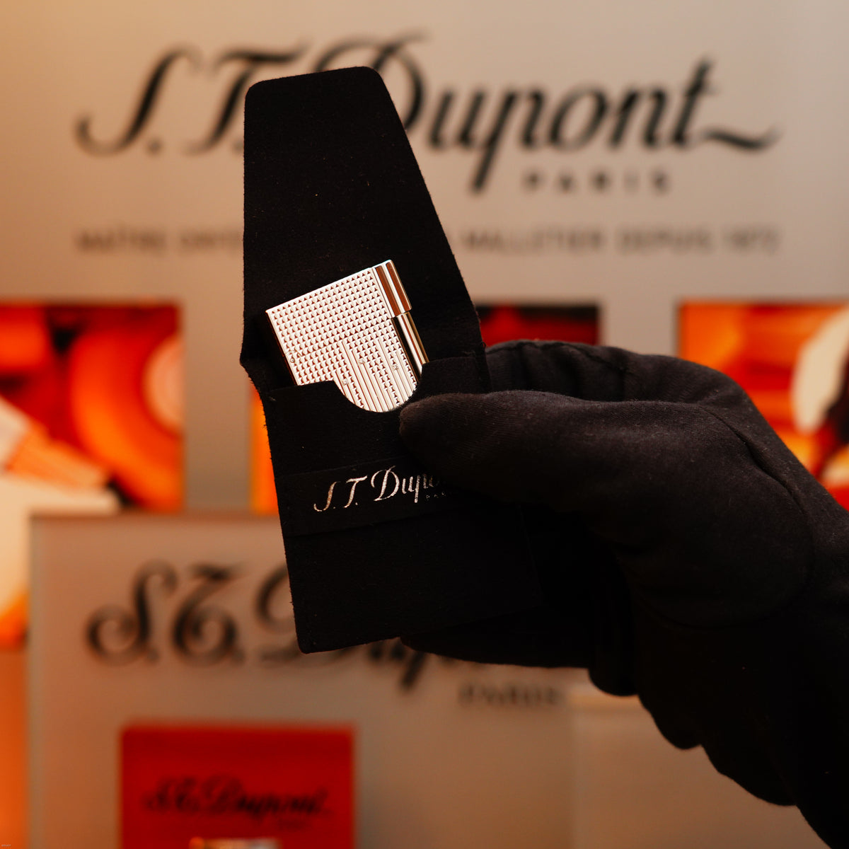 A gloved hand holds a Vintage 2005 S.T. Dupont Gatsby Diamond Drops with 16 Natural Diamond Heavy Platinum Limited Edition Lighter, with S.T. Dupont branding in the background.