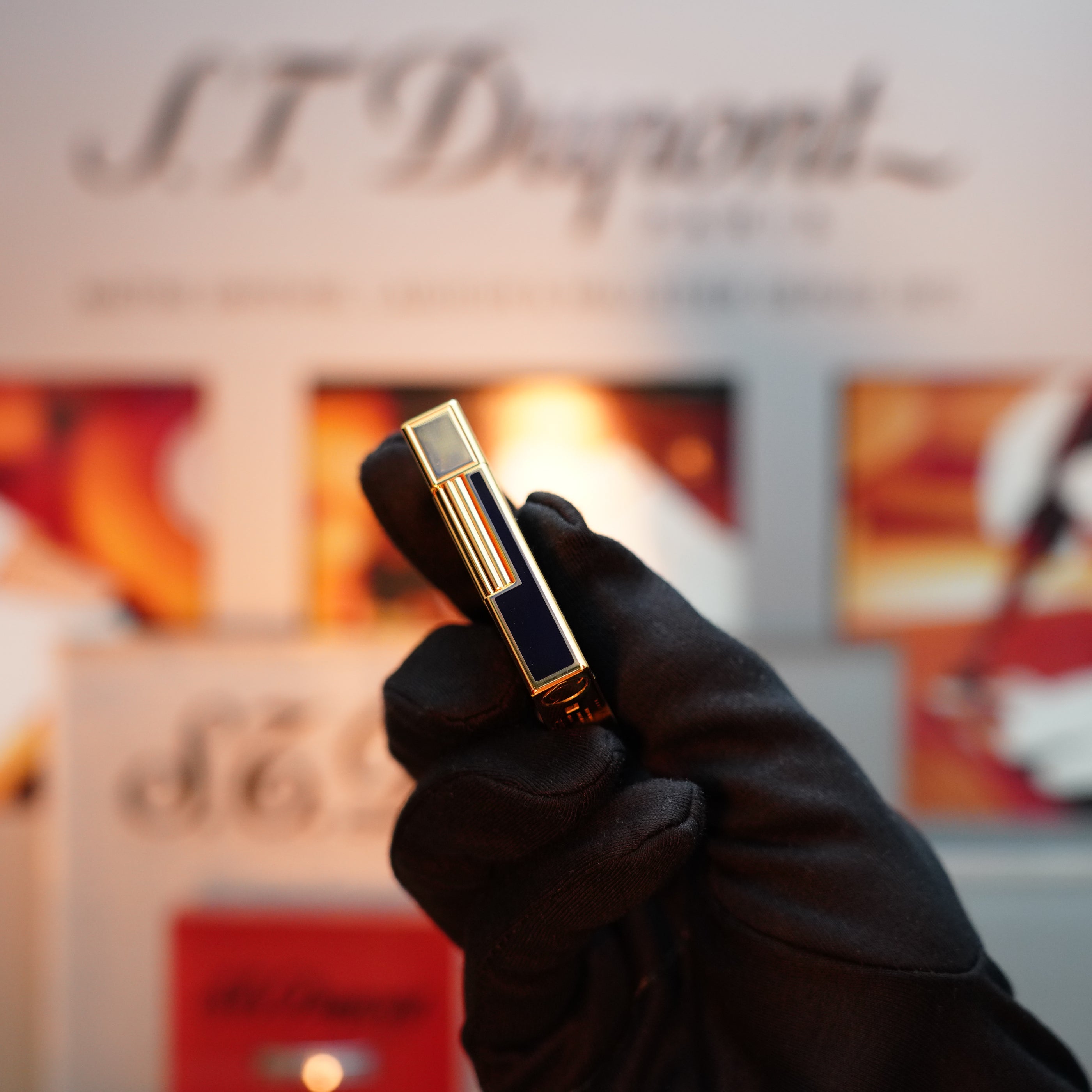 A gloved hand holds a striking gold and black object, the Vintage 1992 S.T. Dupont Important 24k Gold Finish Columbus Gatsby Second Limited Edition Ever Made Lighter, against an elegant S.T. Dupont backdrop.