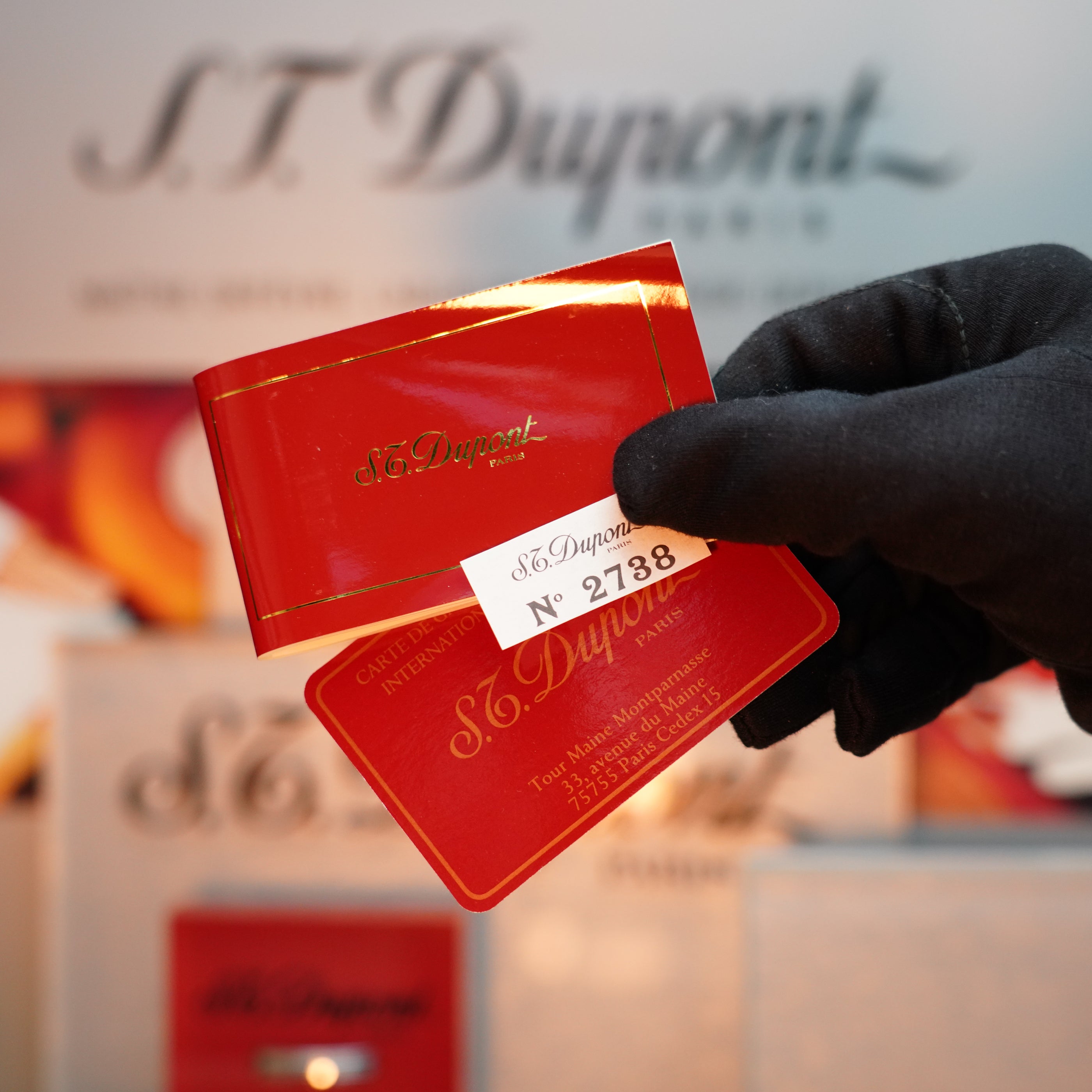 A gloved hand holds a red certificate with gold text from S.T. Dupont, labeled "No. 2738," against a blurred background showcasing the iconic branding of their Vintage 1992 St Dupont Important 24k Gold Finish Colombus Gatsby second Limited Edition ever made Lighter.
