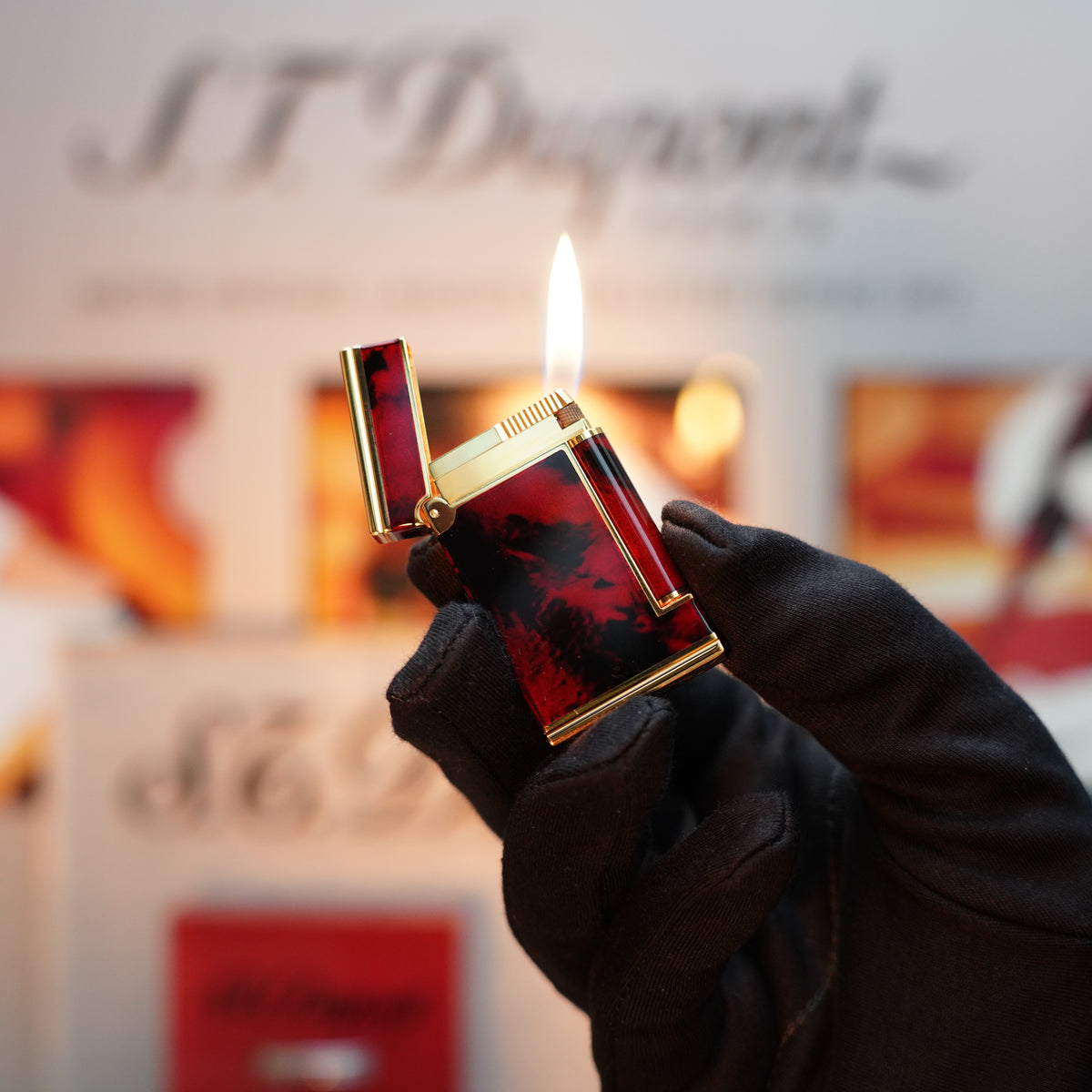 A gloved hand delicately holds a Vintage 1990 S.T. Dupont Iconic D Ligne lighter, featuring a luxurious 24k gold finish and lacquer wheel, displaying a visible flame against a softly blurred background.