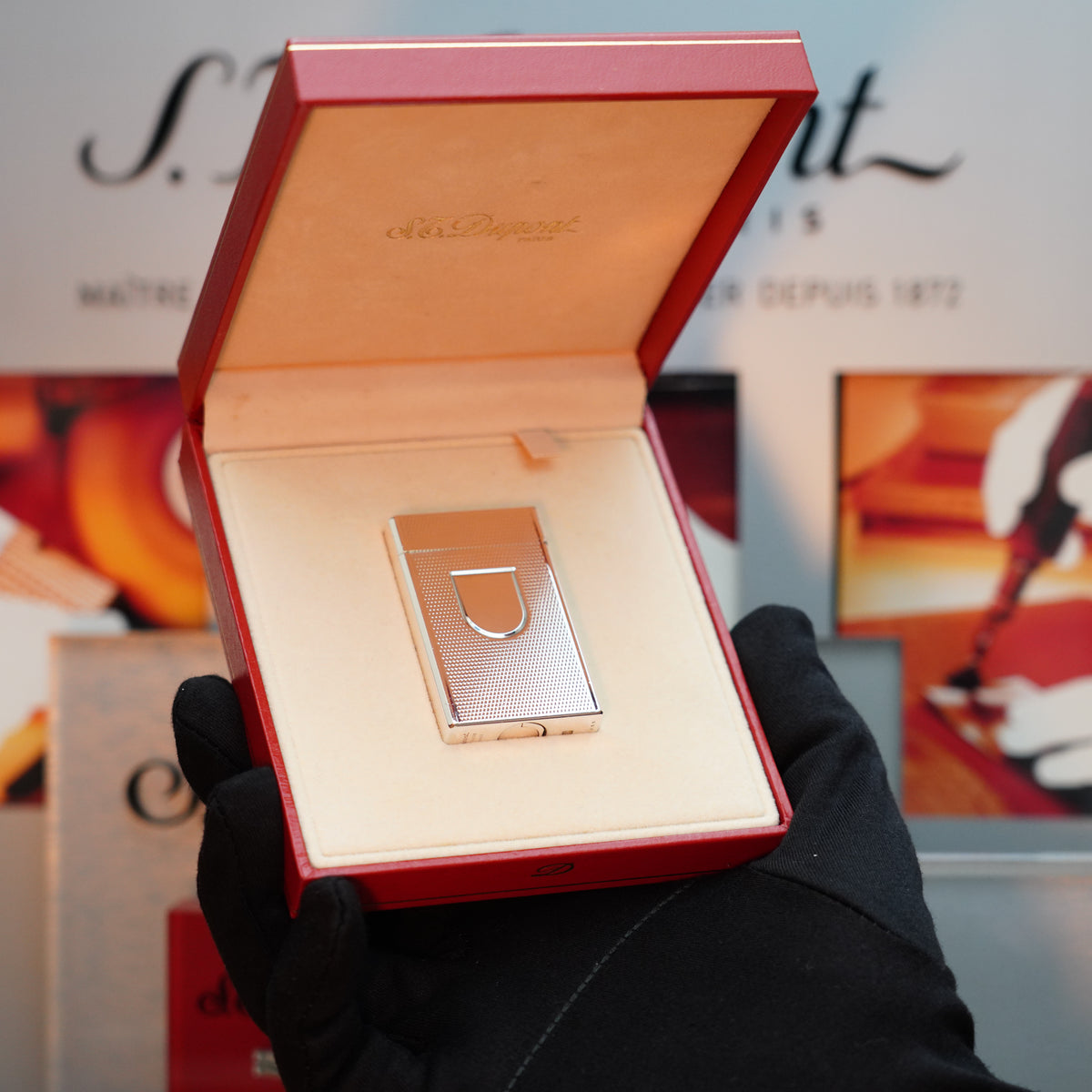 A person wearing a black glove holds an open red box containing a Vintage 1980 S.T. Dupont lighter, featuring a heavy silver finish with a fine hobnail pattern and adorned with the Ecusson "D" logo.