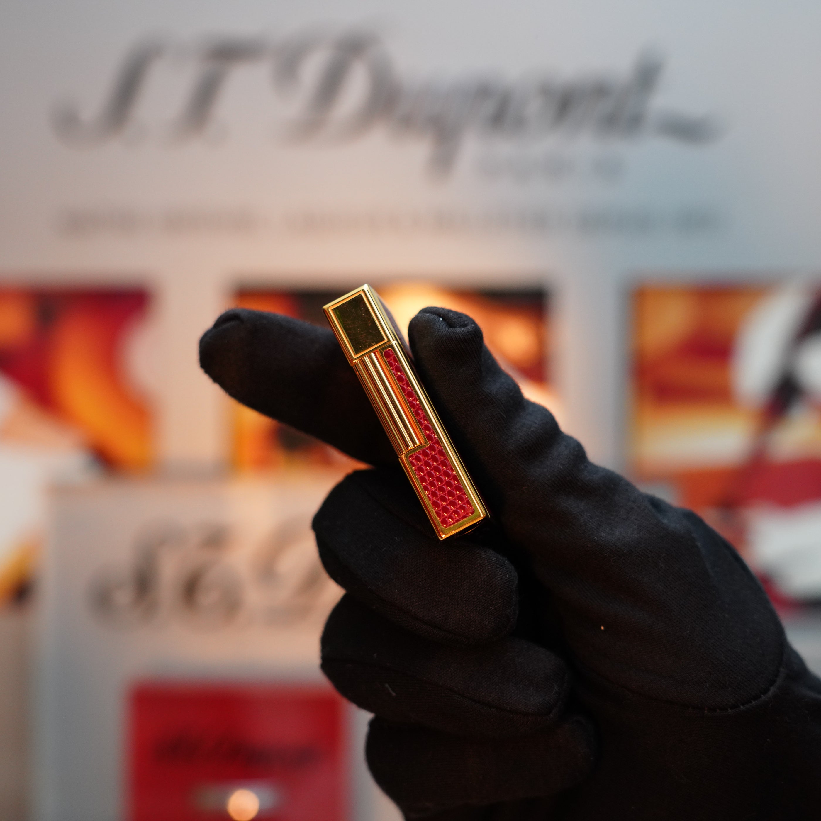 A gloved hand holds a Vintage 1980 S.T. Dupont Gatsby Gainerie Lezard Red Bordeaux Authentic leather lighter with a 24k gold finish against a blurred background showcasing the S.T. Dupont logo.