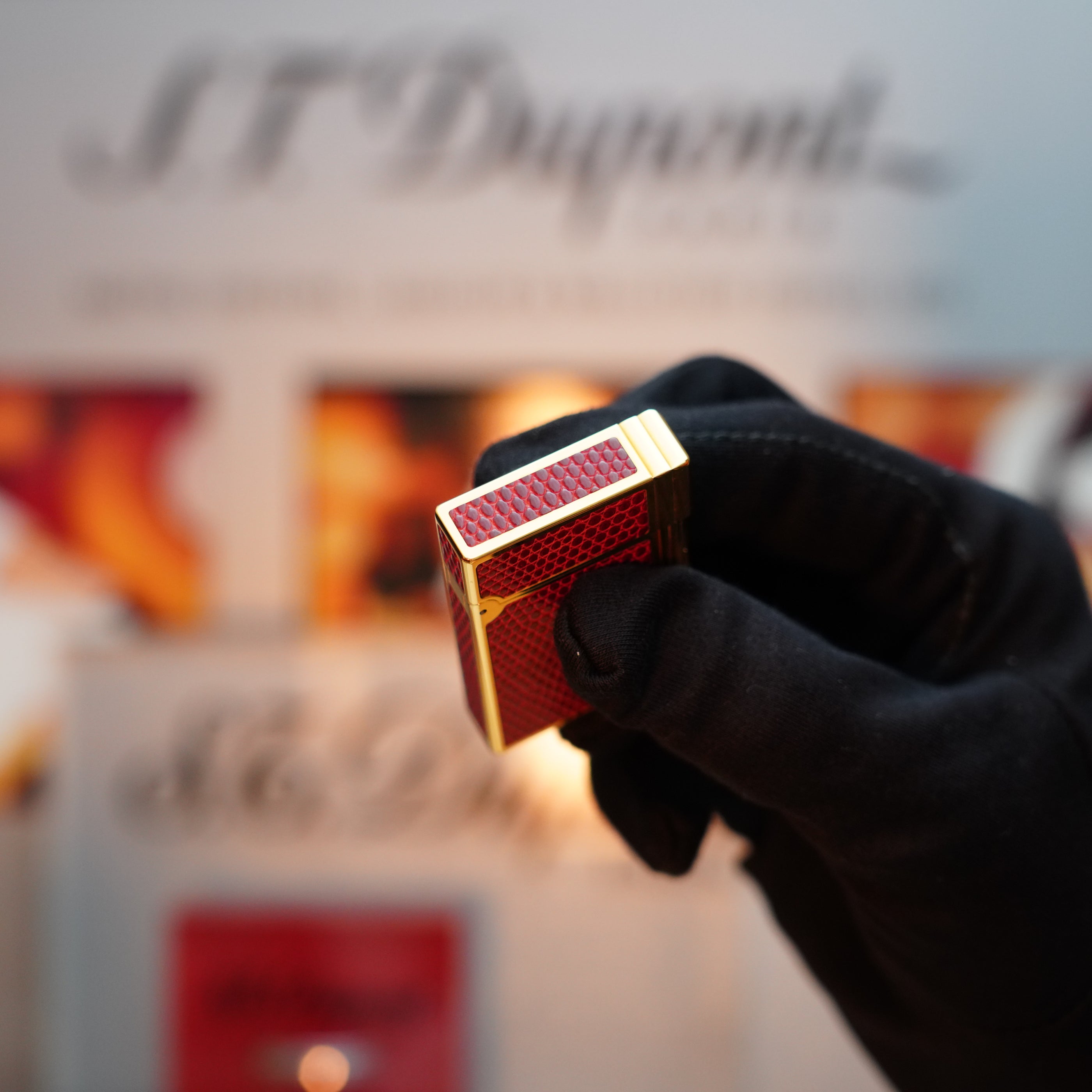 A gloved hand holds the Vintage 1980 S.T. Dupont 24k Gold finish Gatsby Gainerie Lezard Lighter in Red Bordeaux, with blurred branding visible in the background, evoking the elegance of a rare vintage piece.