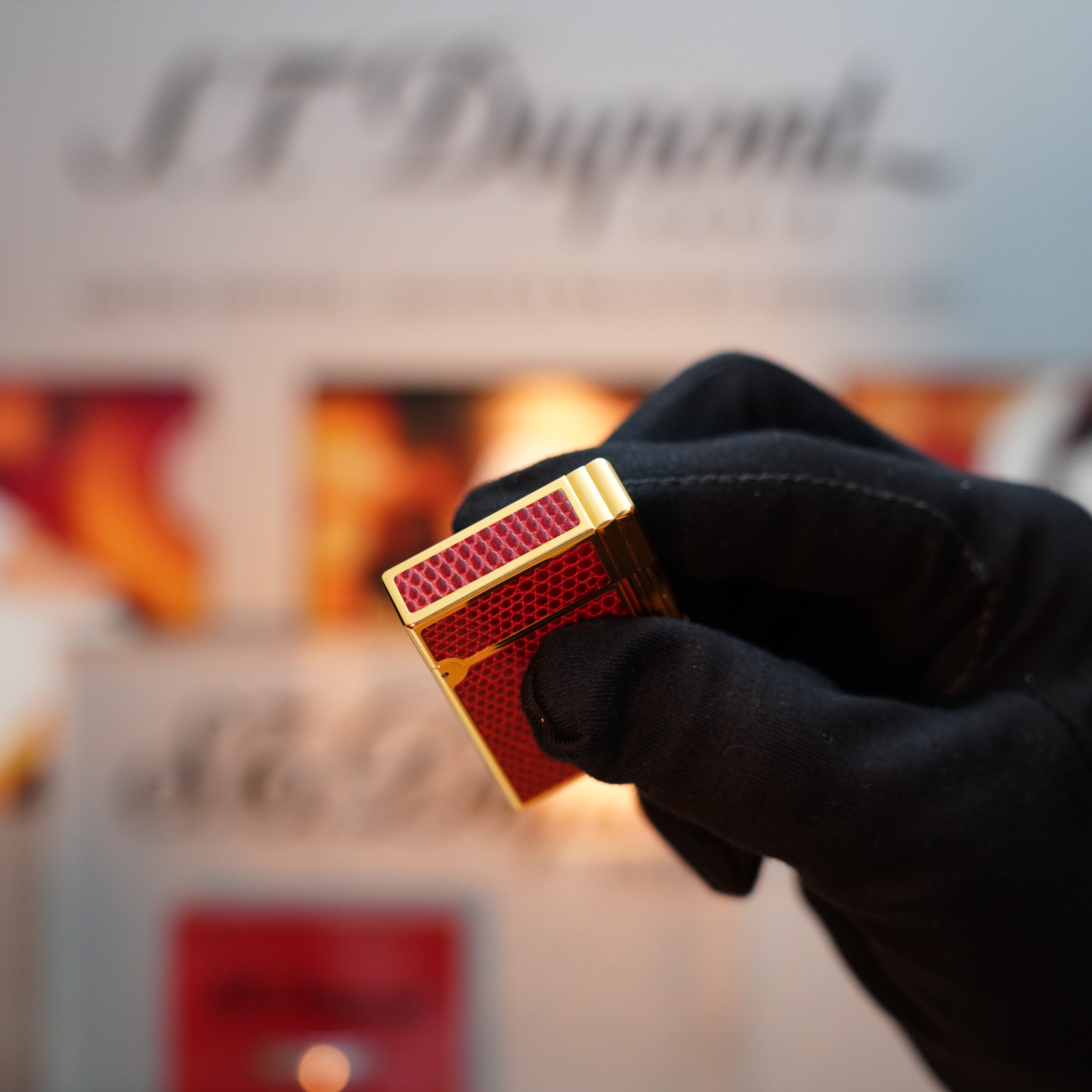 A person wearing black gloves holds the Vintage 1980 St Dupont Gatsby Gainerie Lezard Red Bordeaux lighter, an exceptionally rare rectangular object with a 24k gold finish against a blurred background displaying the text "S.T. Dupont.