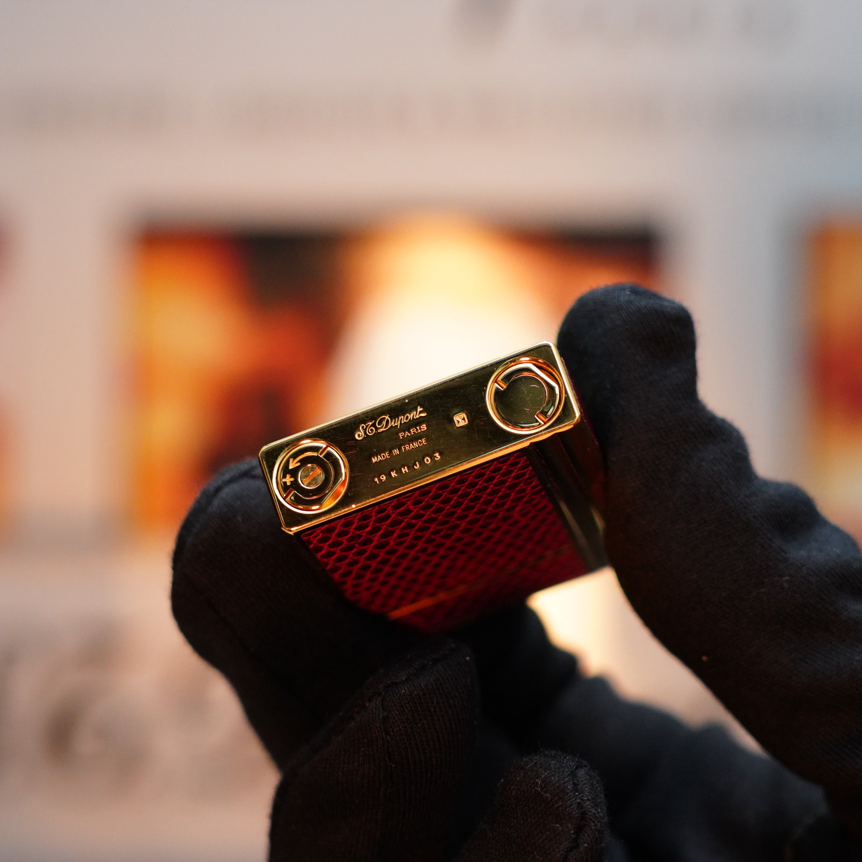 A gloved hand holds a vintage 1980 S.T. Dupont Gatsby Gainerie Lezard lighter, featuring an exquisite red Bordeaux and 24k gold finish and authentic leather design, with the cap open to reveal its two rounded ignition areas.