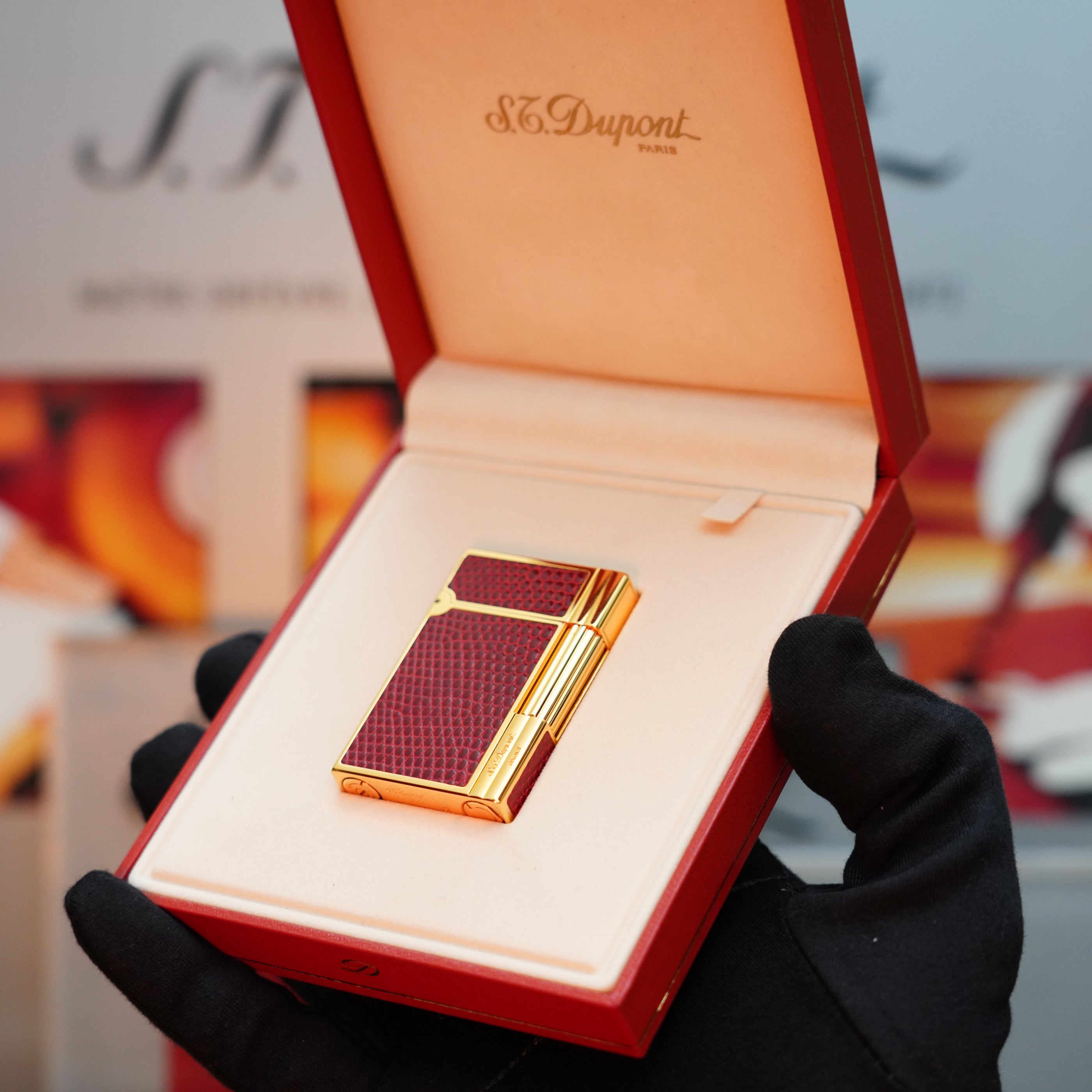 A gloved hand holds a Vintage 1980 S.T. Dupont Gatsby Gainerie Lezard lighter with a 24k gold finish, elegantly nestled in its authentic red Bordeaux leather display box.