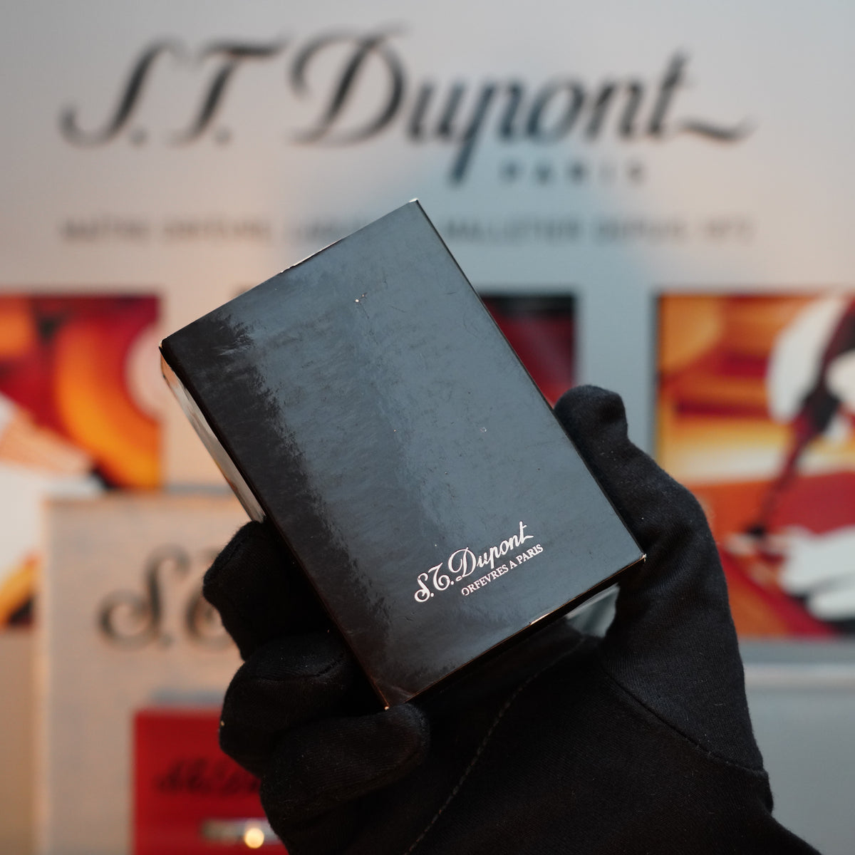 A gloved hand holds a black S.T. Dupont box, unveiling the elegant allure of a Vintage 1990 St Dupont Limited Edition Vertigo Gatsby Ligne 2 lighter in its luxurious 24k gold finish.