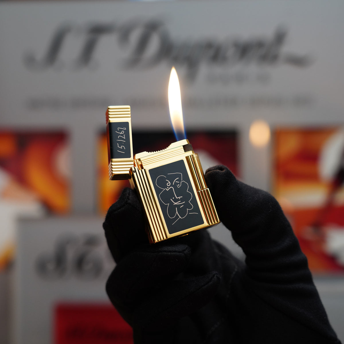A person wearing a black glove holds the Vintage 1990 Important S.T. Dupont Pablo Picasso Limited Edition Ligne 1 lighter, featuring a 24k gold finish and black lacquer design, in front of a blurred background displaying "S.T. Dupont.