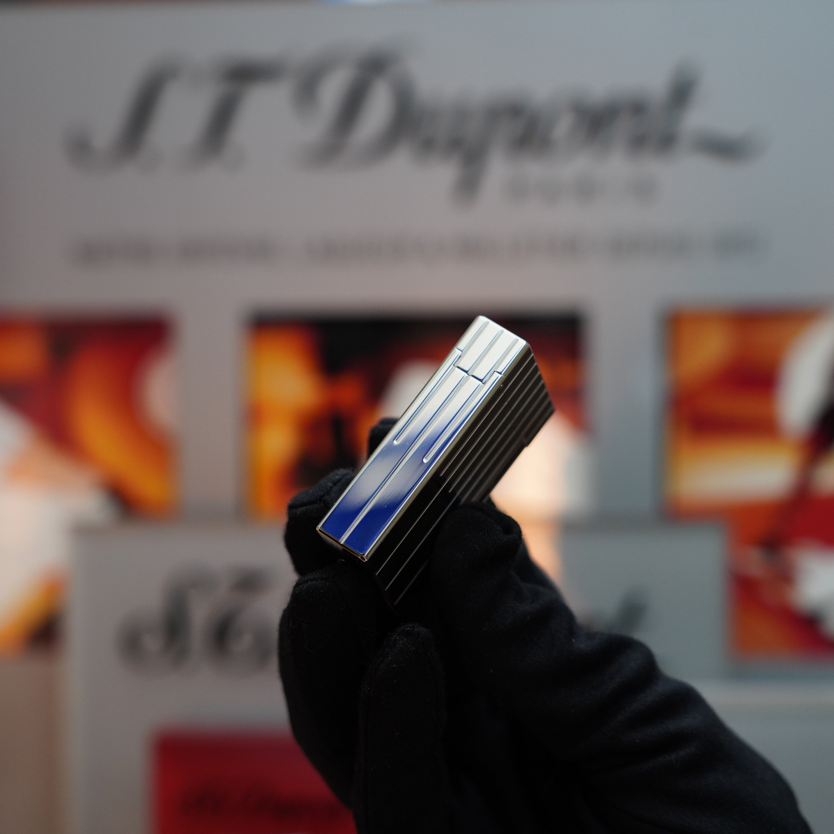 A gloved hand holds a sleek, rectangular metal object with blue and silver detailing—an exquisite Vintage 1999 St Dupont Rare Perspective 2000 Palladium Limited Edition Ligne 1 Lighter—against a blurred background featuring the text "S.T. Dupont.