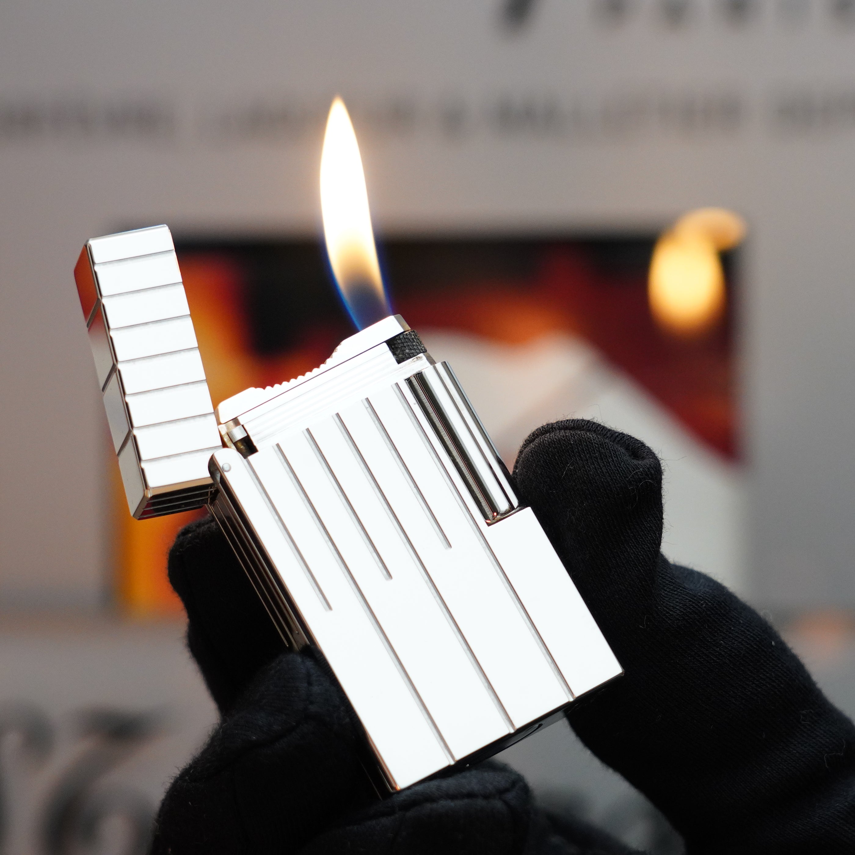 A gloved hand elegantly holds an open Vintage 1999 St Dupont Rare Perspective 2000 Palladium Limited Edition Ligne 1 Lighter by S.T. Dupont, showcasing its lit flame against a blurred background.