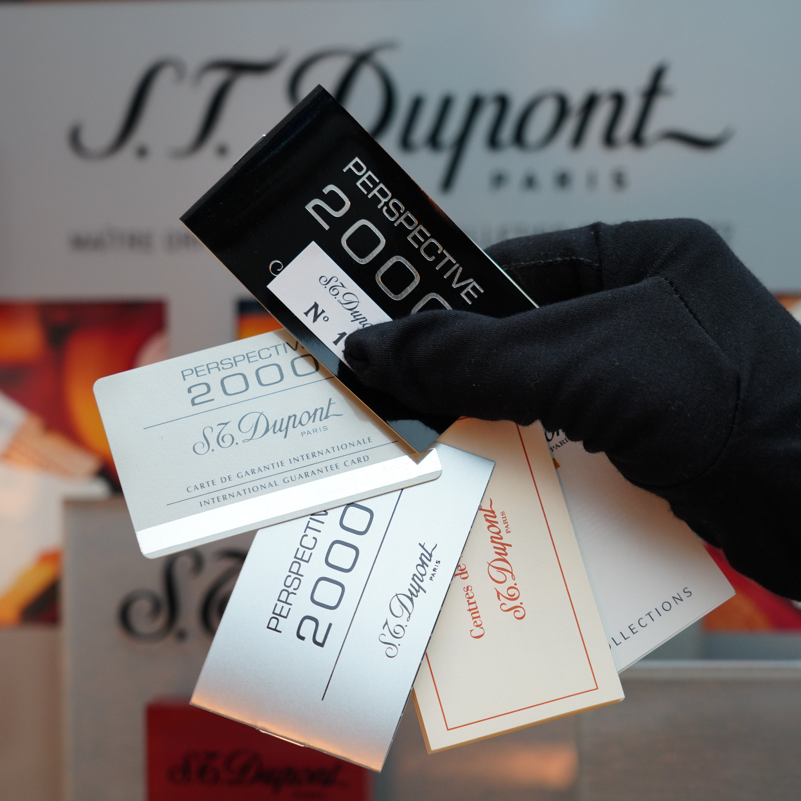 A gloved hand holds several S.T. Dupont guarantee cards in an array of colors, such as black and silver, suggesting the sophistication of a Vintage 1999 St Dupont Rare Perspective 2000 Palladium Limited Edition Ligne 1 Lighter.