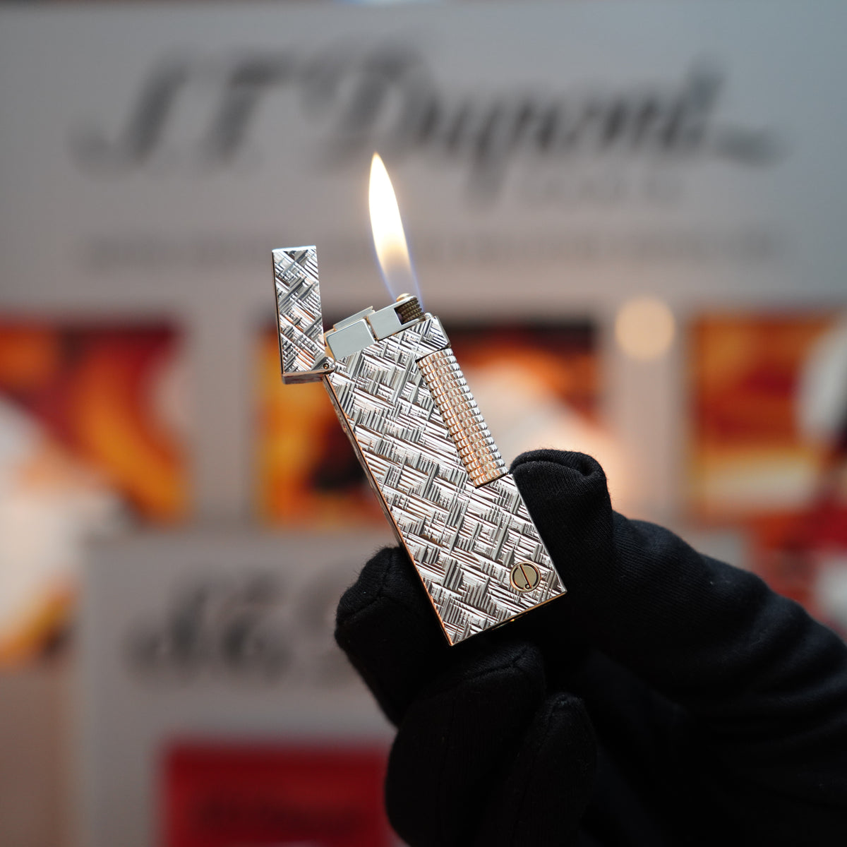 A hand holds a Vintage 1980 Dunhill D line Rollagas Cross Hatch Heavy Silver Finish rare Lighter, its flame casting a soft glow against the blurred background.