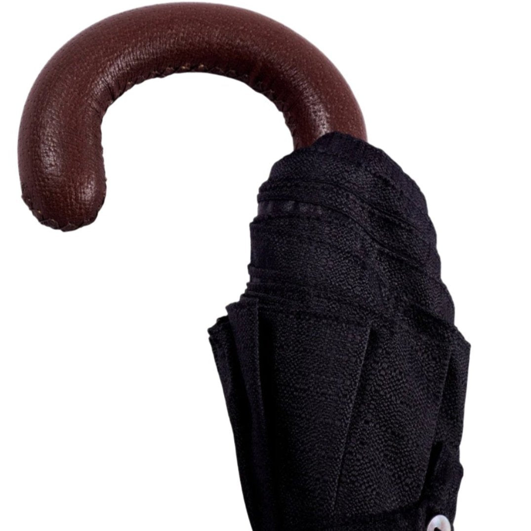 A KirbyAllison.com brown pigskin travel umbrella with black canopy and a brown handle.