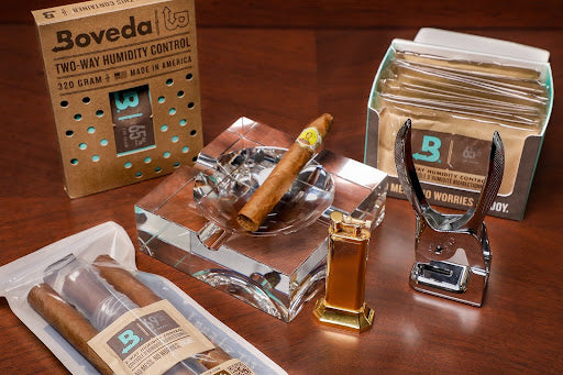 Various cigar accessories such as humidor bags, an ash tray, cigar cutter, etc., set up on a table 