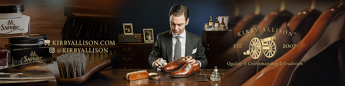 A man in a suit polishes a brown leather dress shoe at a desk, surrounded by leather care products and the Kirby Allison logo.