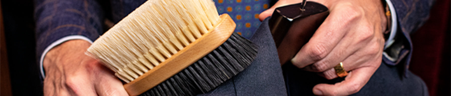 A man polishes brown leather shoes at a desk surrounded by shoe care products. The text reads "Kirby Allison" with website and social media handles.