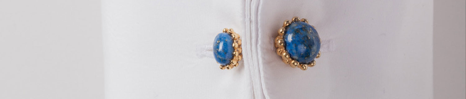 Close-up of a white dress shirt cuff with gold and blue stone cufflinks fastened through the buttonholes.